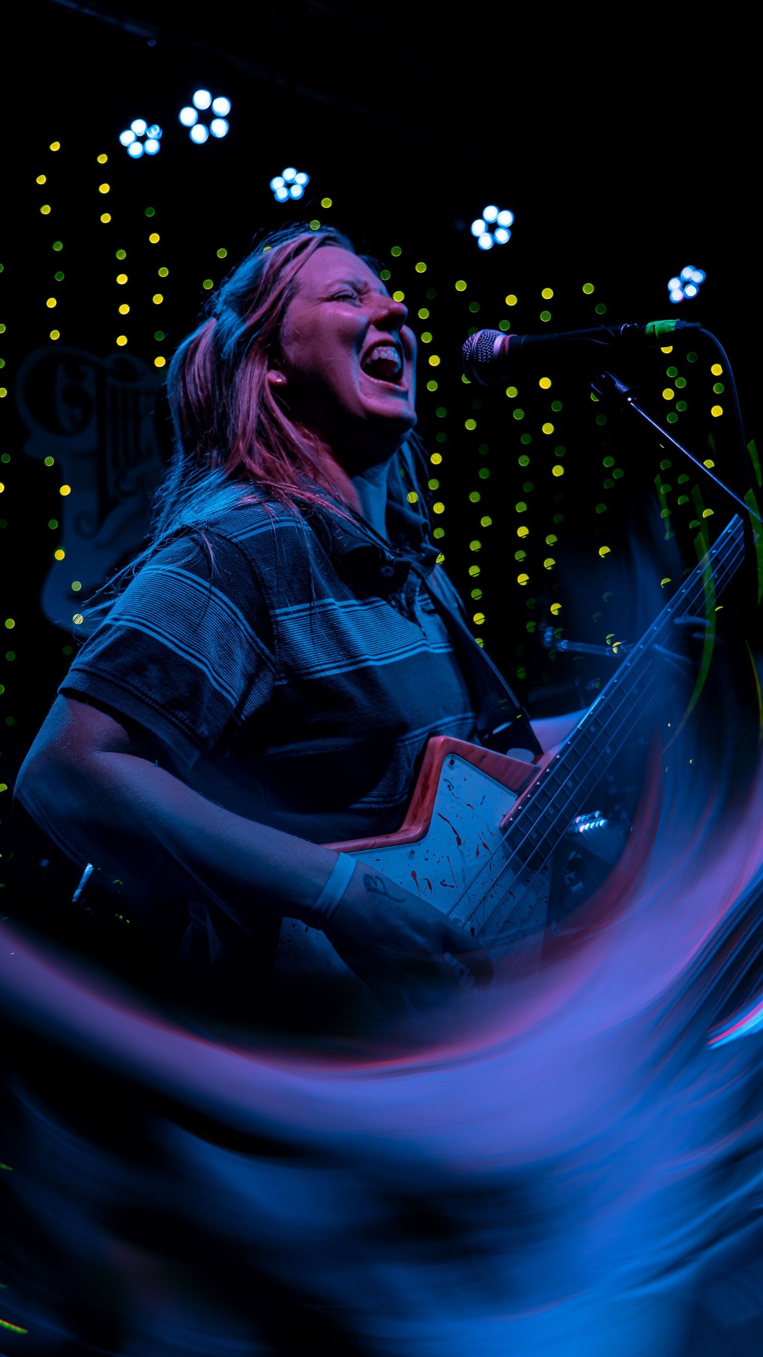 Vocalist performing passionately on stage with dramatic blue lighting and bokeh effects in the background.
