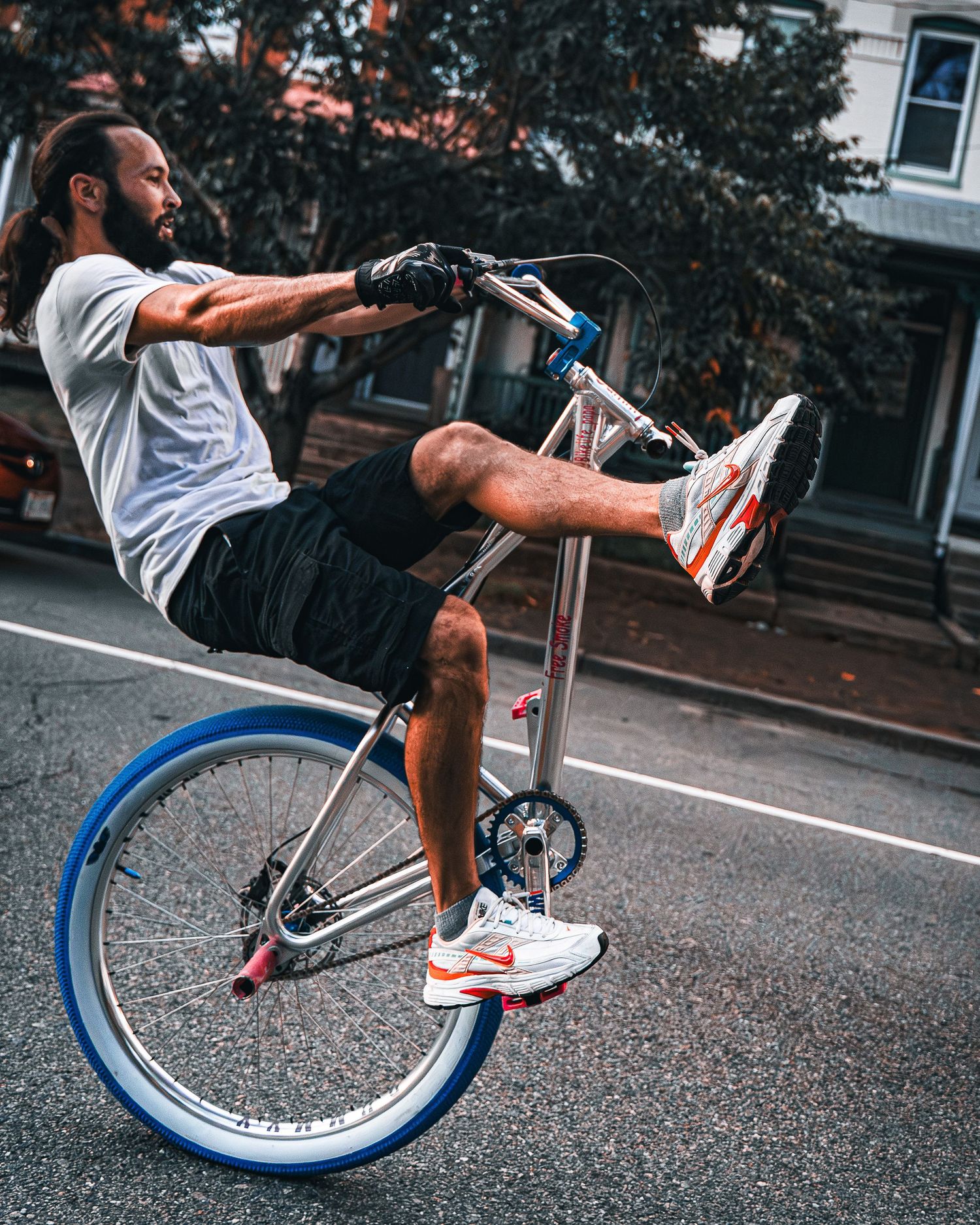 Cyclist performs manual balance trick on blue bike in urban street setting.