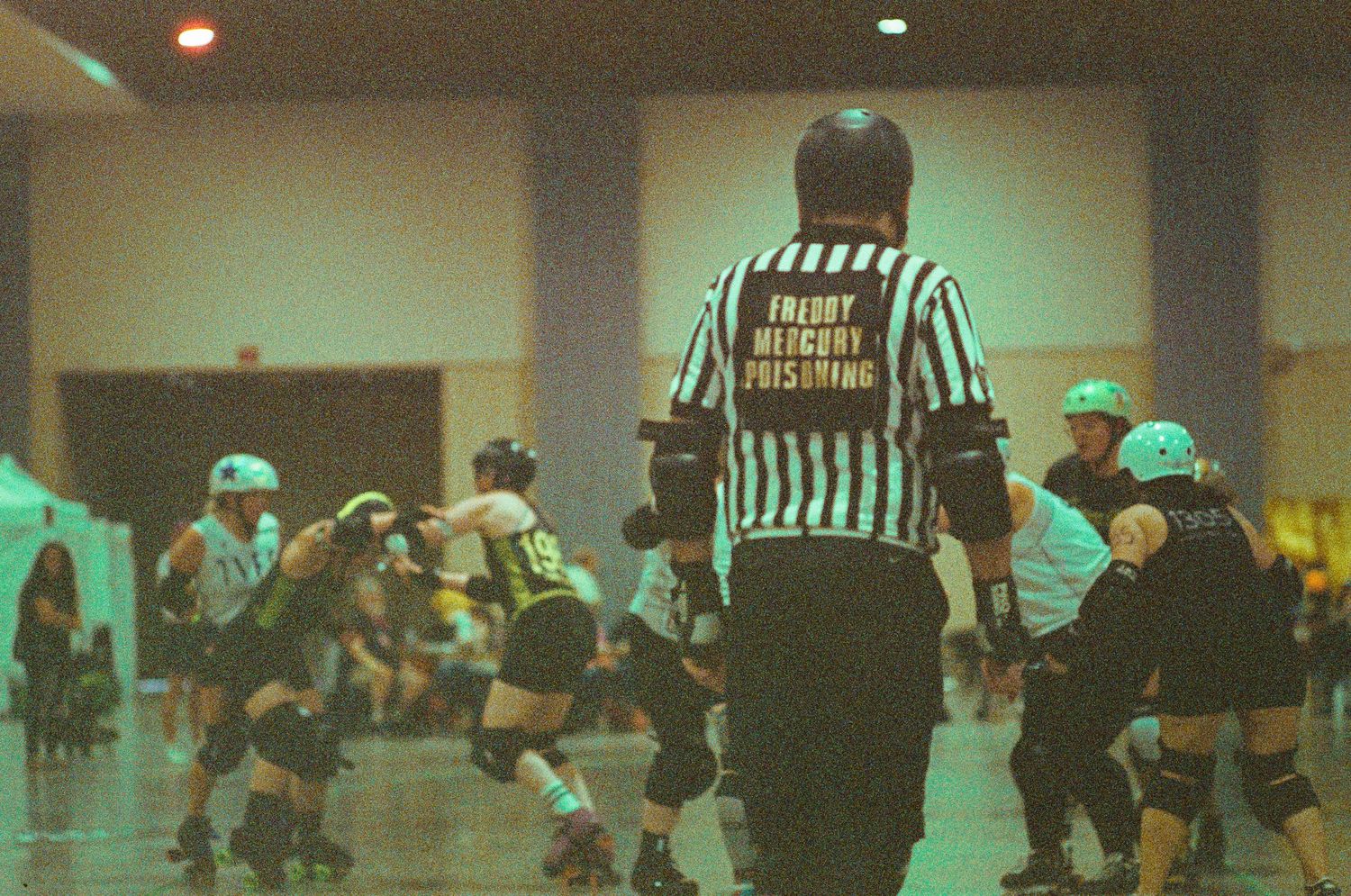 Wide shot of indoor sports event with referees and players on court under fluorescent lighting.