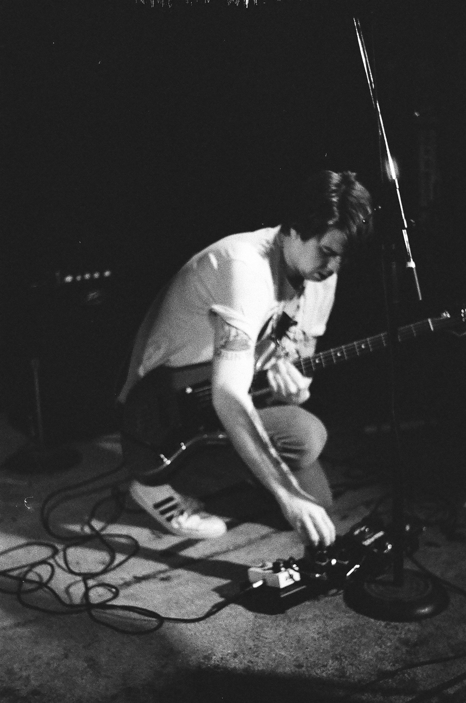 Black and white image of musician adjusting equipment on stage floor.