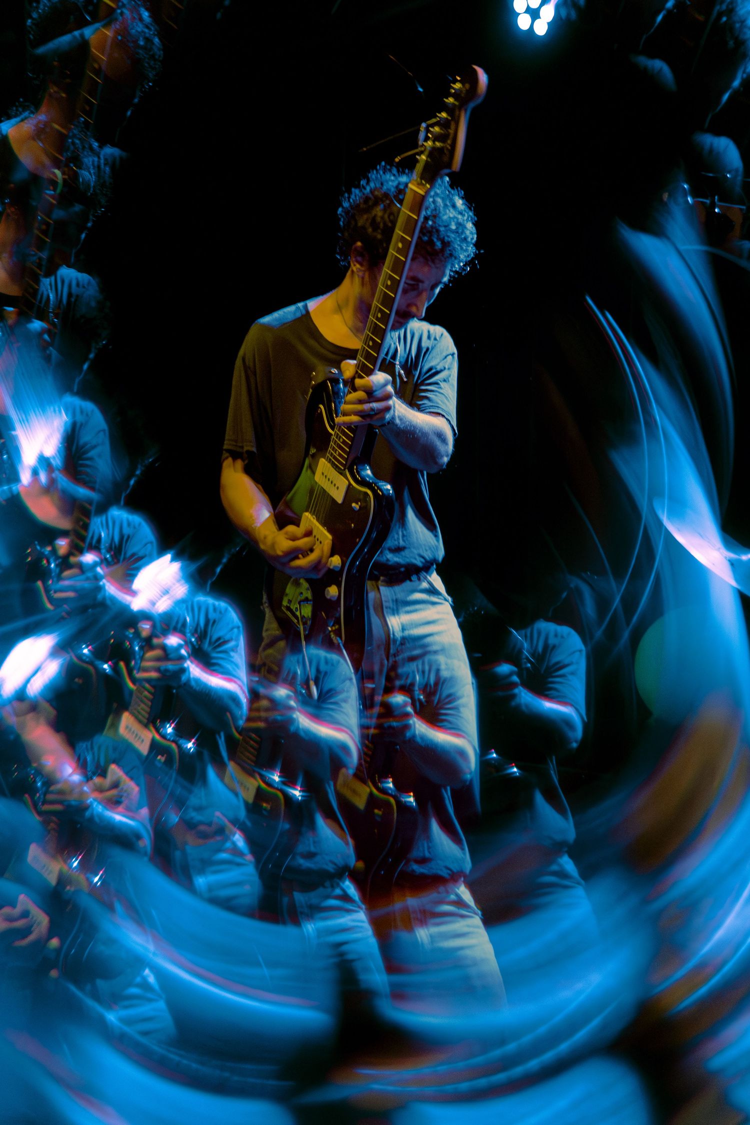 Motion-blurred musicians perform on stage with electric guitars against a dark background illuminated by dramatic blue lighting.