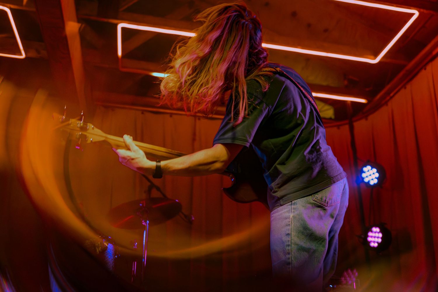 Person with colorful hair performing on stage with dramatic lighting and vibrant neon effects in a concert setting.