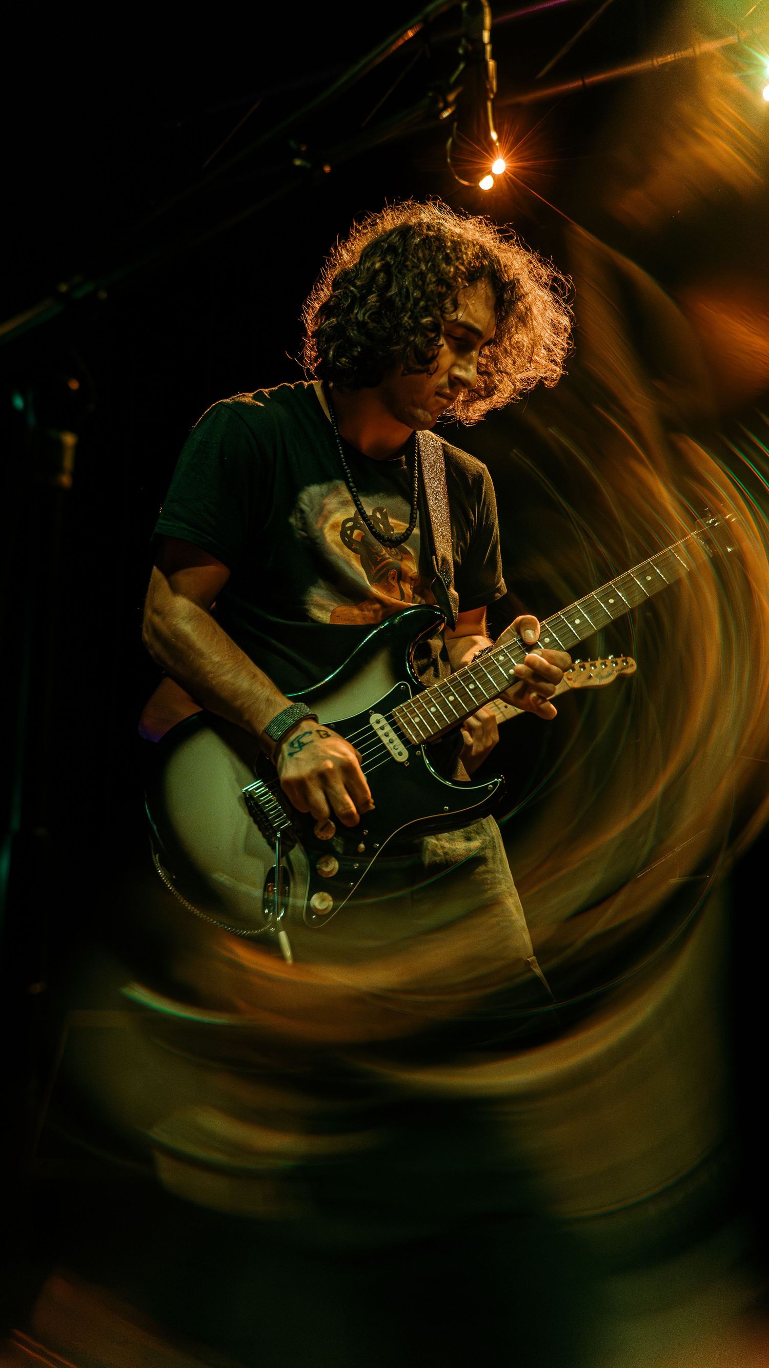 Guitarist playing electric guitar captured in swirling motion blur effect under dramatic stage lighting.