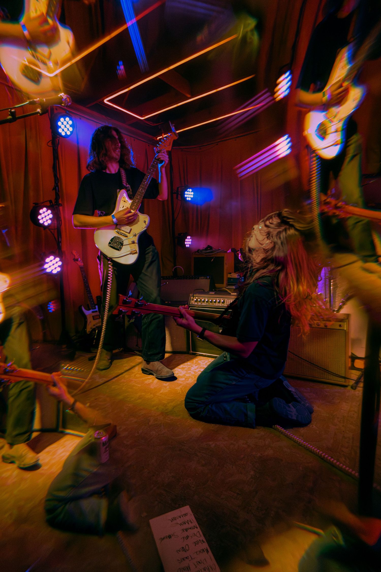 Musician performs on acoustic guitar in dimly lit venue with colorful purple and orange stage lighting.