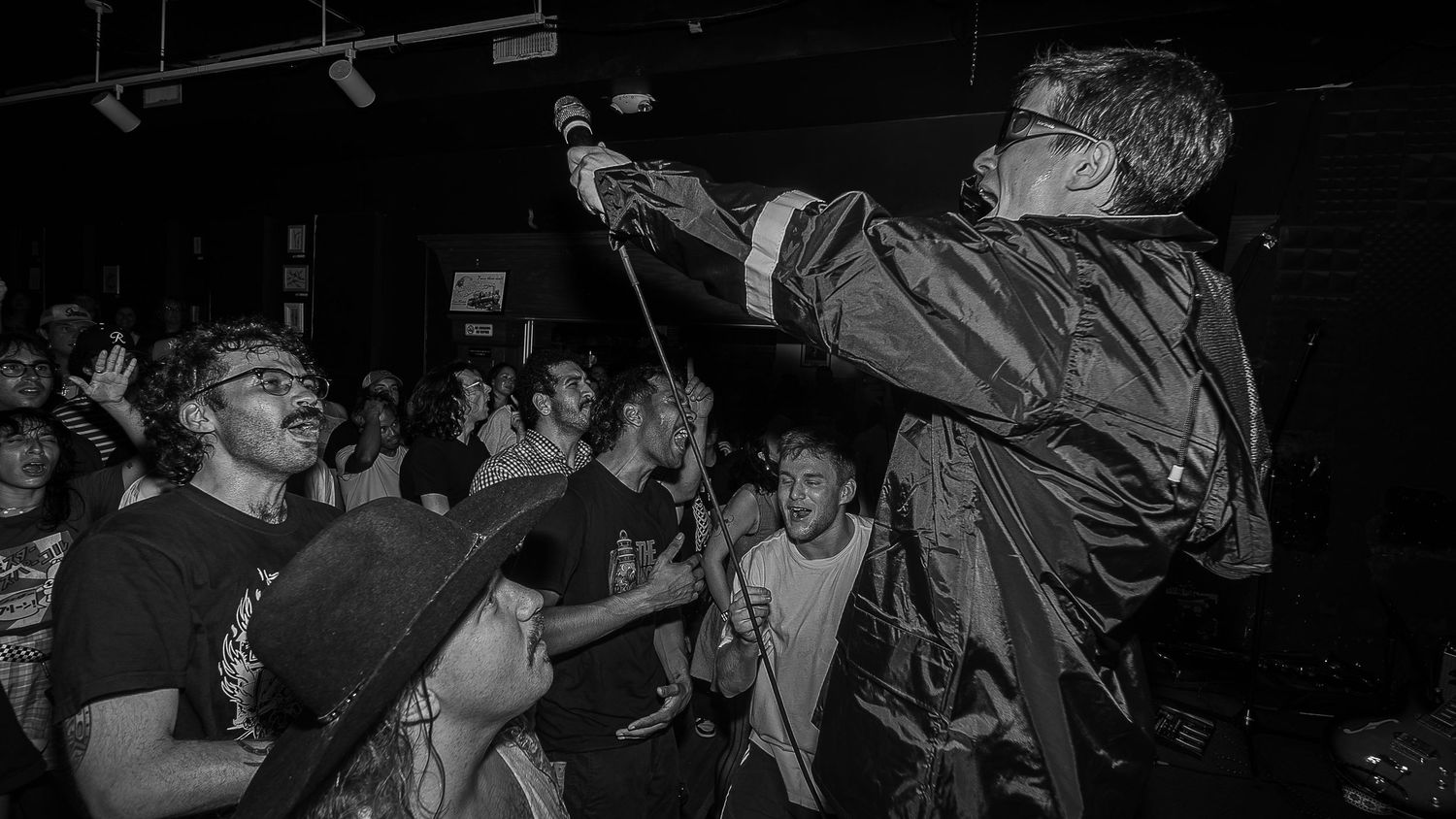 A lively concert crowd waves their hands in the air during a nighttime performance at a music venue.