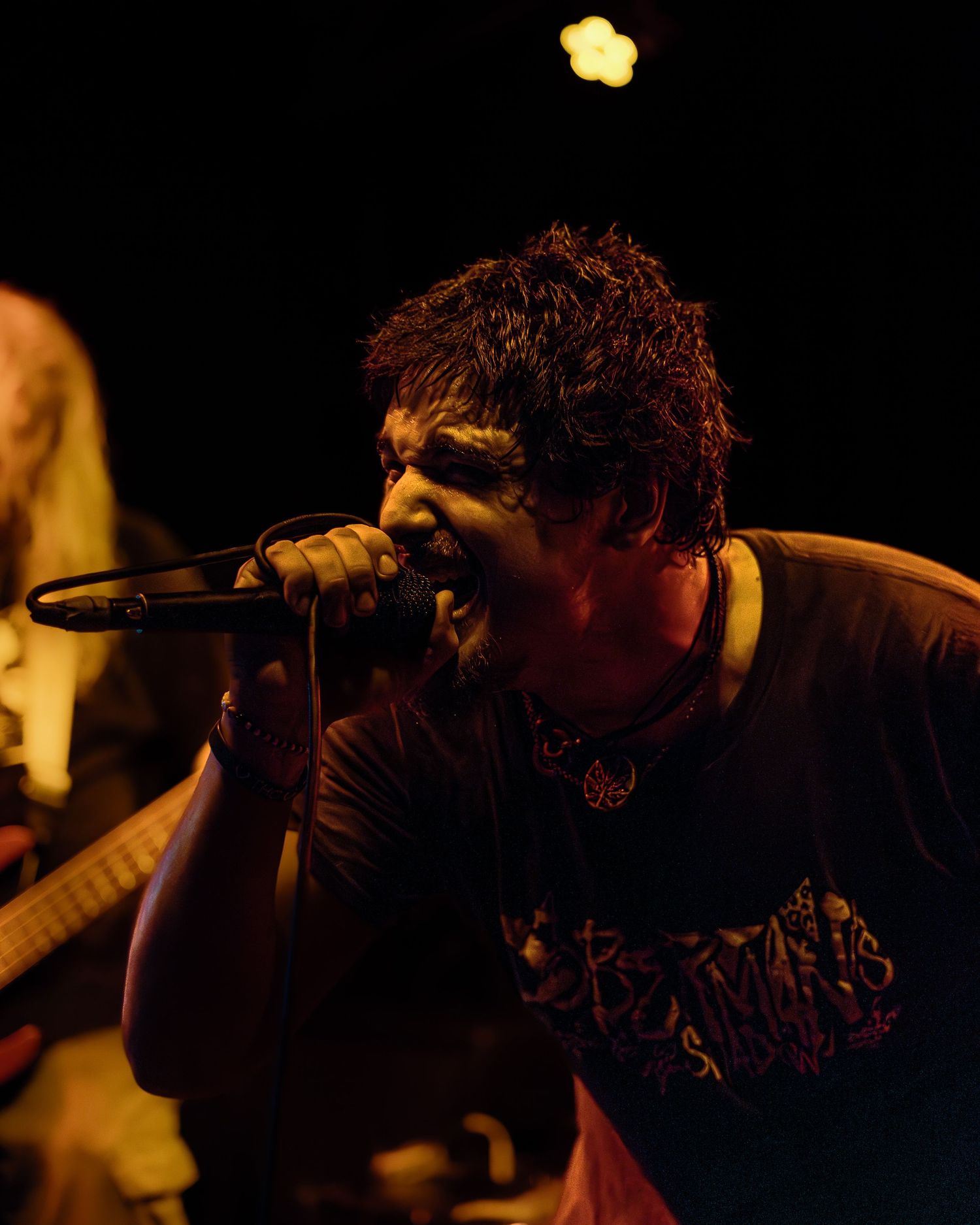 A performer singing passionately into a microphone on a darkly lit stage with dramatic amber lighting.