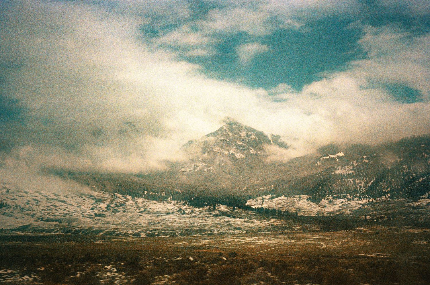 Misty mountain peak rises above a barren valley landscape under dramatic cloudy skies.