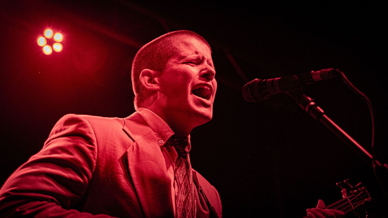 Stage performer singing emotionally under intense red spotlight during live performance.