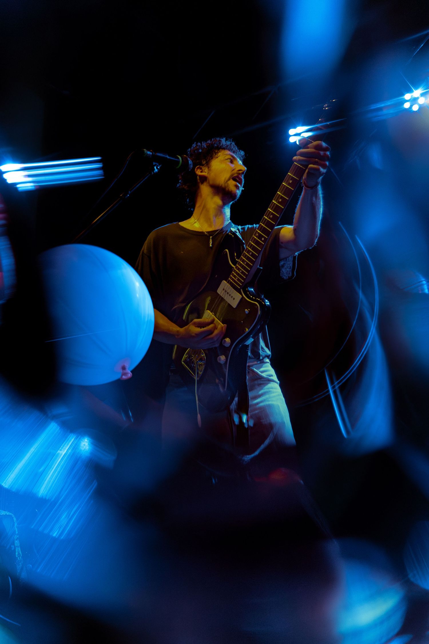 A performer with a guitar plays passionately on stage under dramatic blue lighting at a concert.