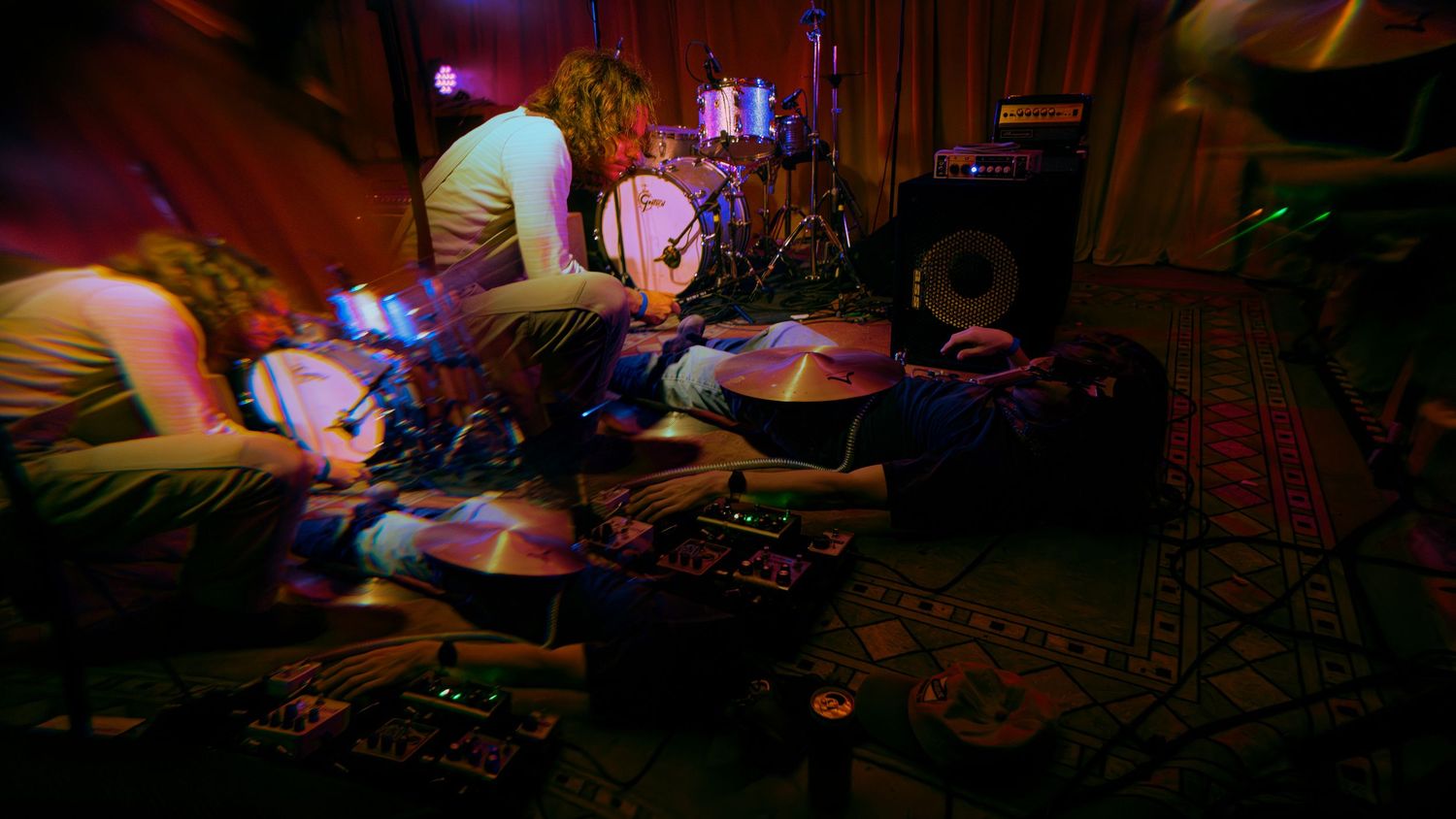 Musicians perform at a dimly lit concert venue with neon lighting effects and electronic equipment.