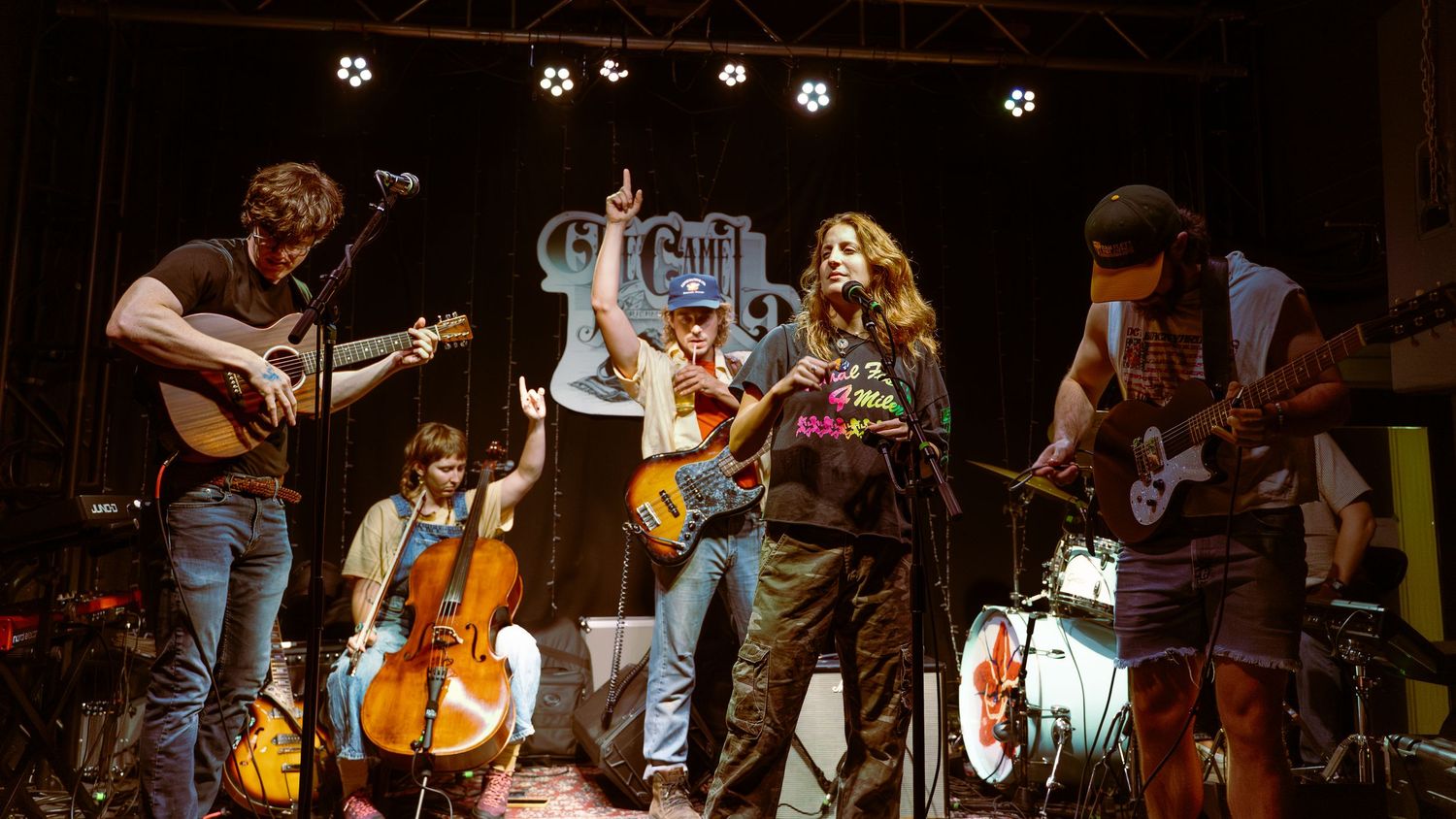 Musicians perform on stage during a folk music concert with string instruments and lighting effects in the background.