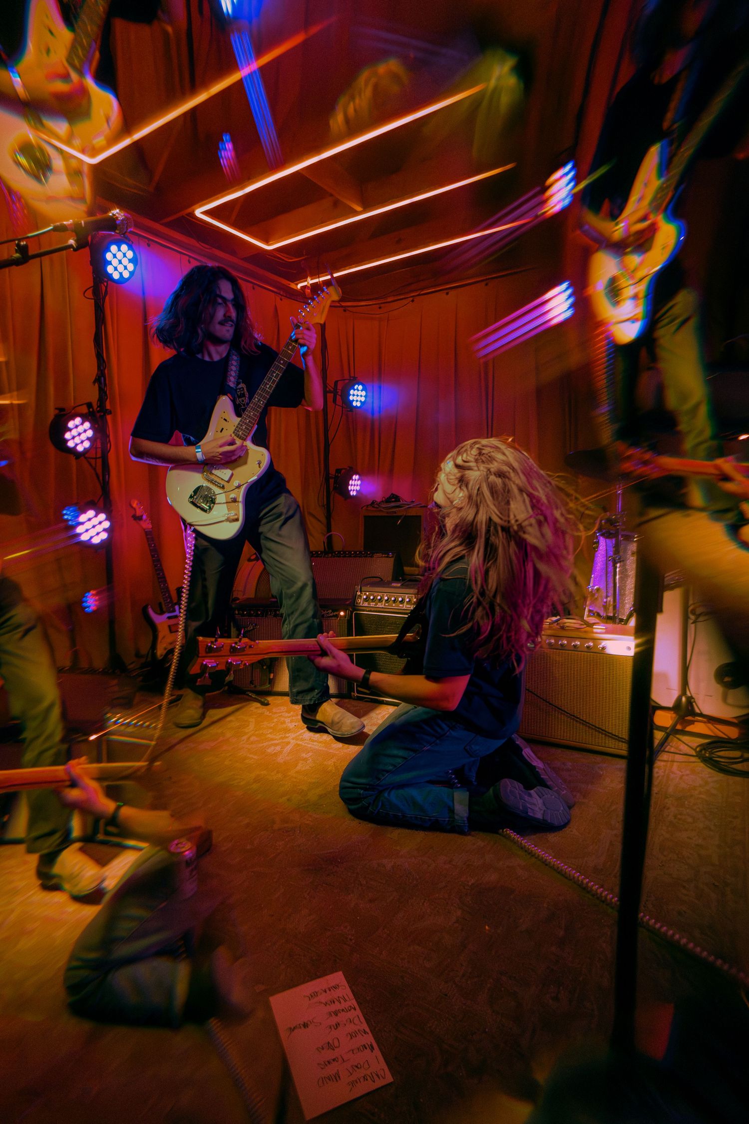 Musicians perform in a dimly lit studio space with vibrant blue and red lighting creating an intimate atmosphere.