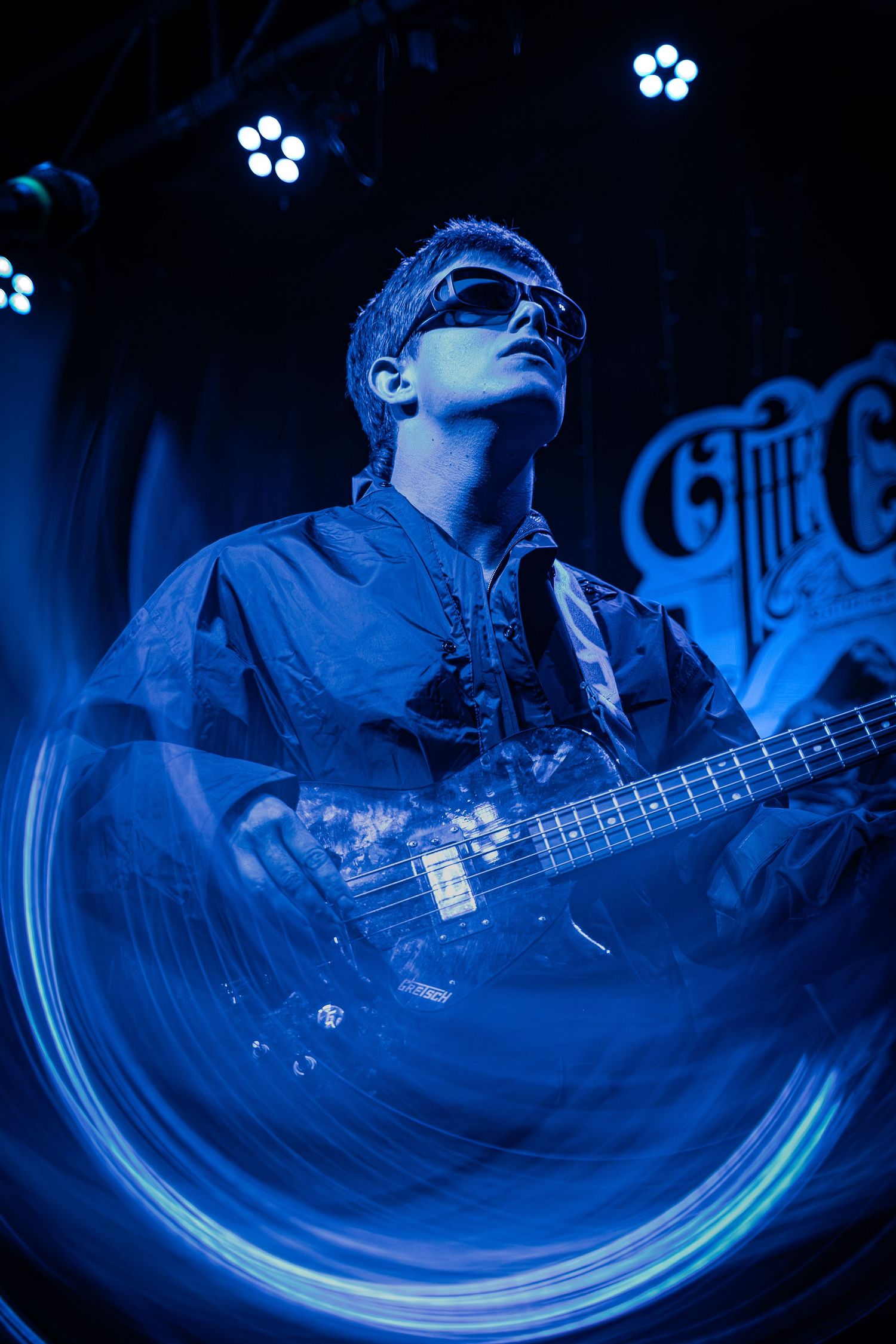 A bassist performs on stage bathed in dramatic blue lighting with a fisheye lens effect creating a circular distortion.