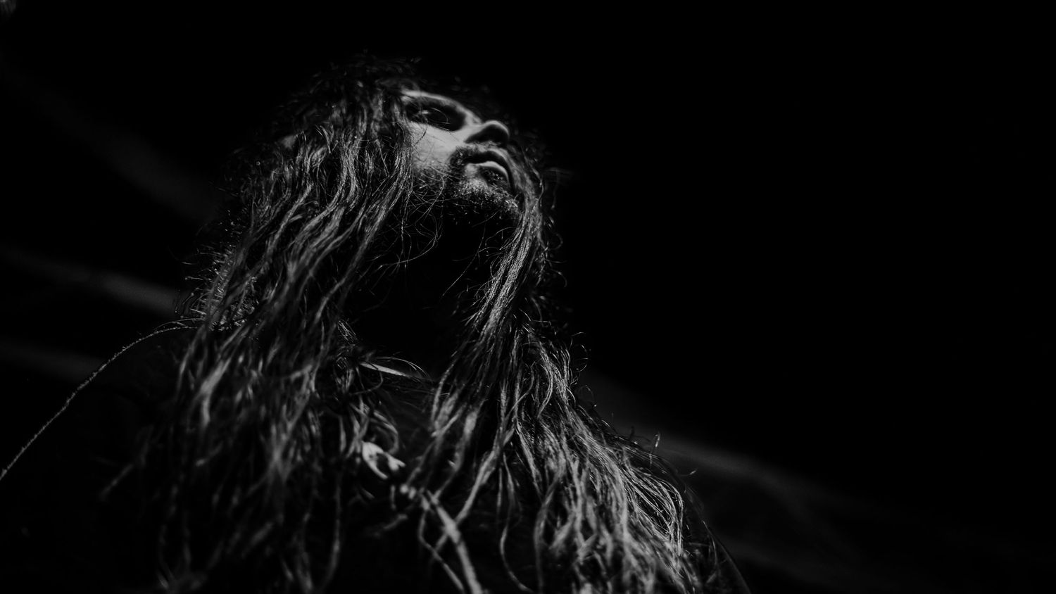 Black and white photo of a person with long hair singing passionately on stage with their head tilted back.