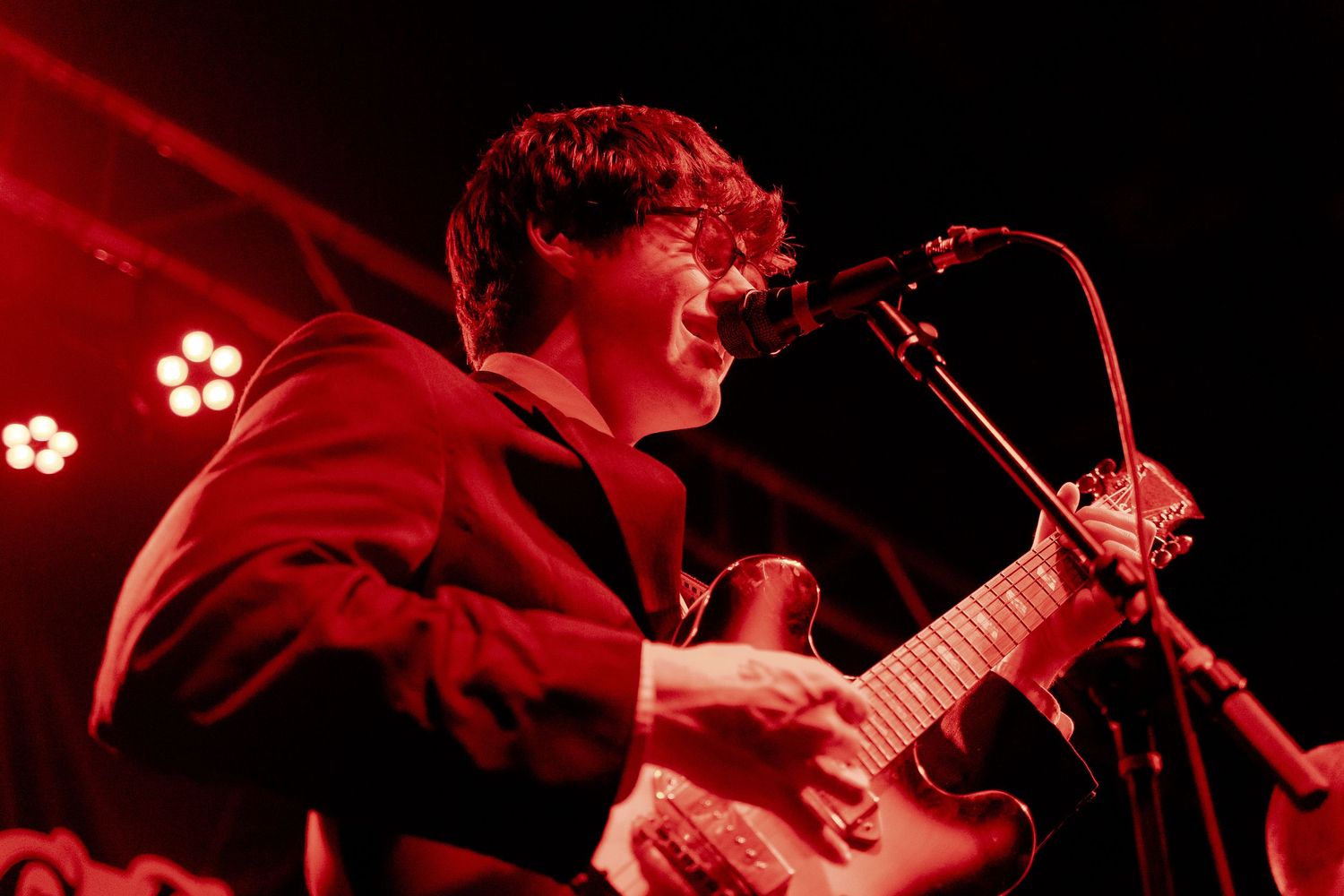 Guitarist bathed in red stage lighting performs passionately during a live concert.