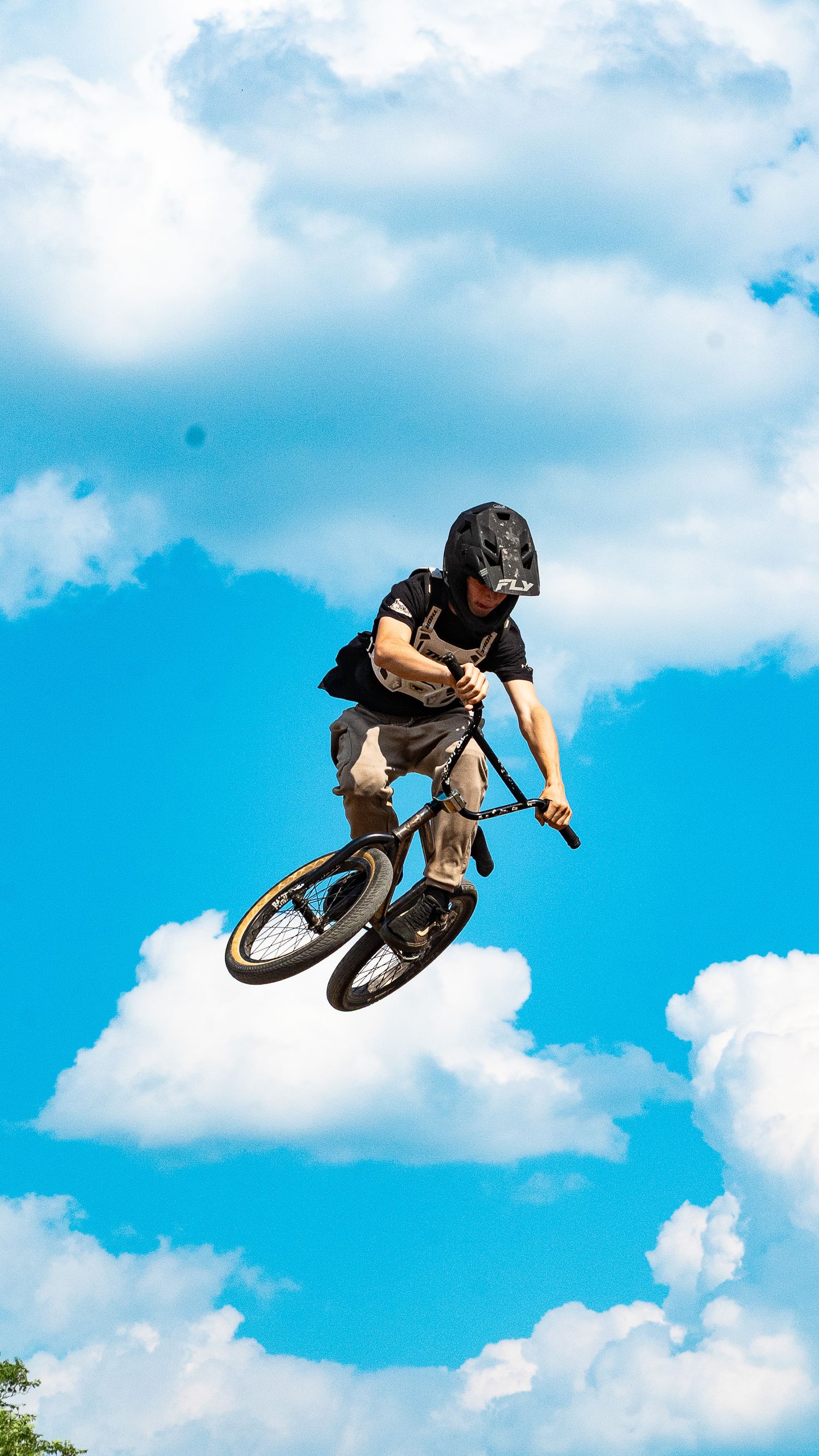 Daredevil BMX rider catches air off a jump while performing tricks against cloudy blue sky.