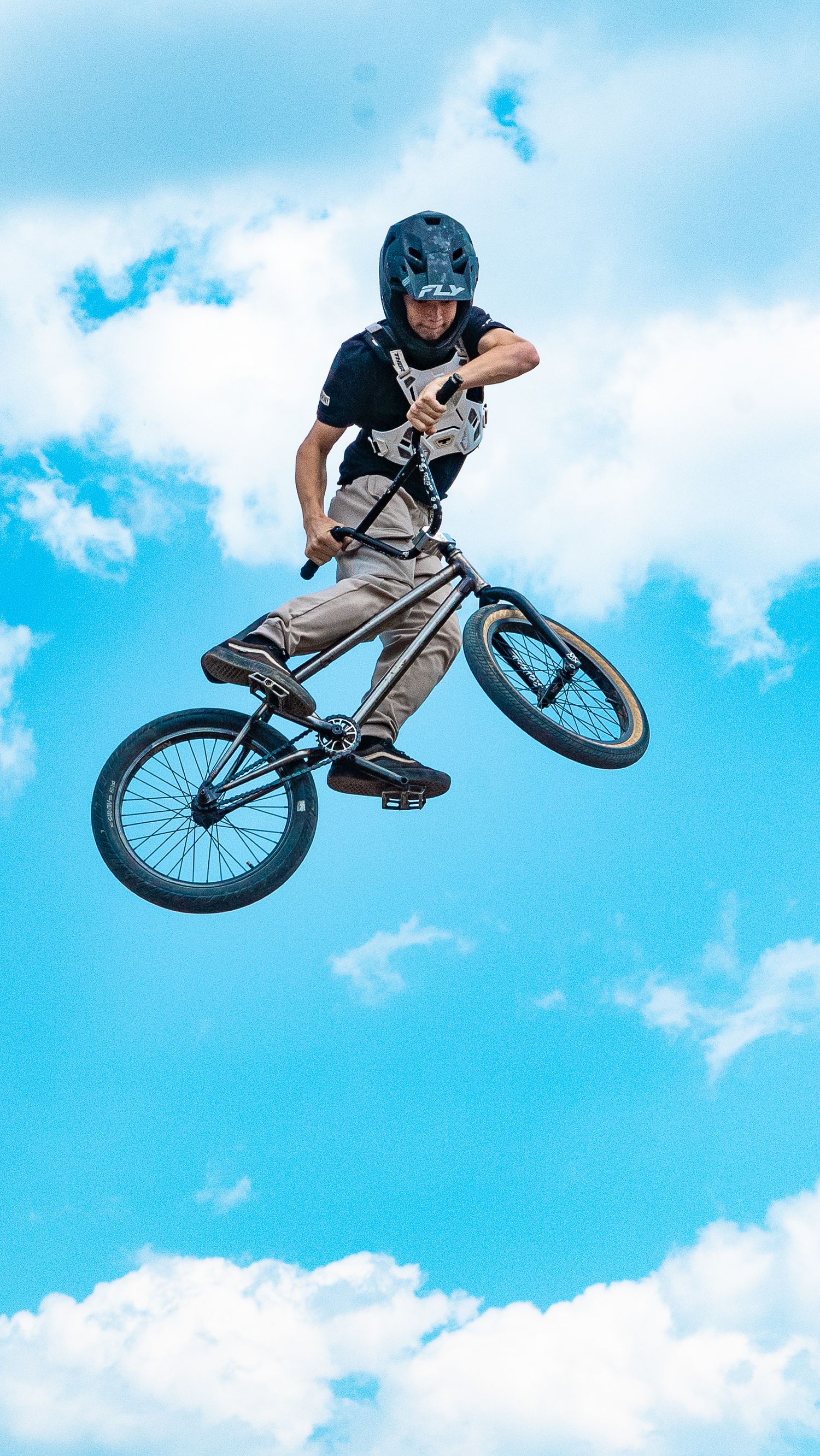 BMX rider performs aerial trick sequence against blue sky backdrop.