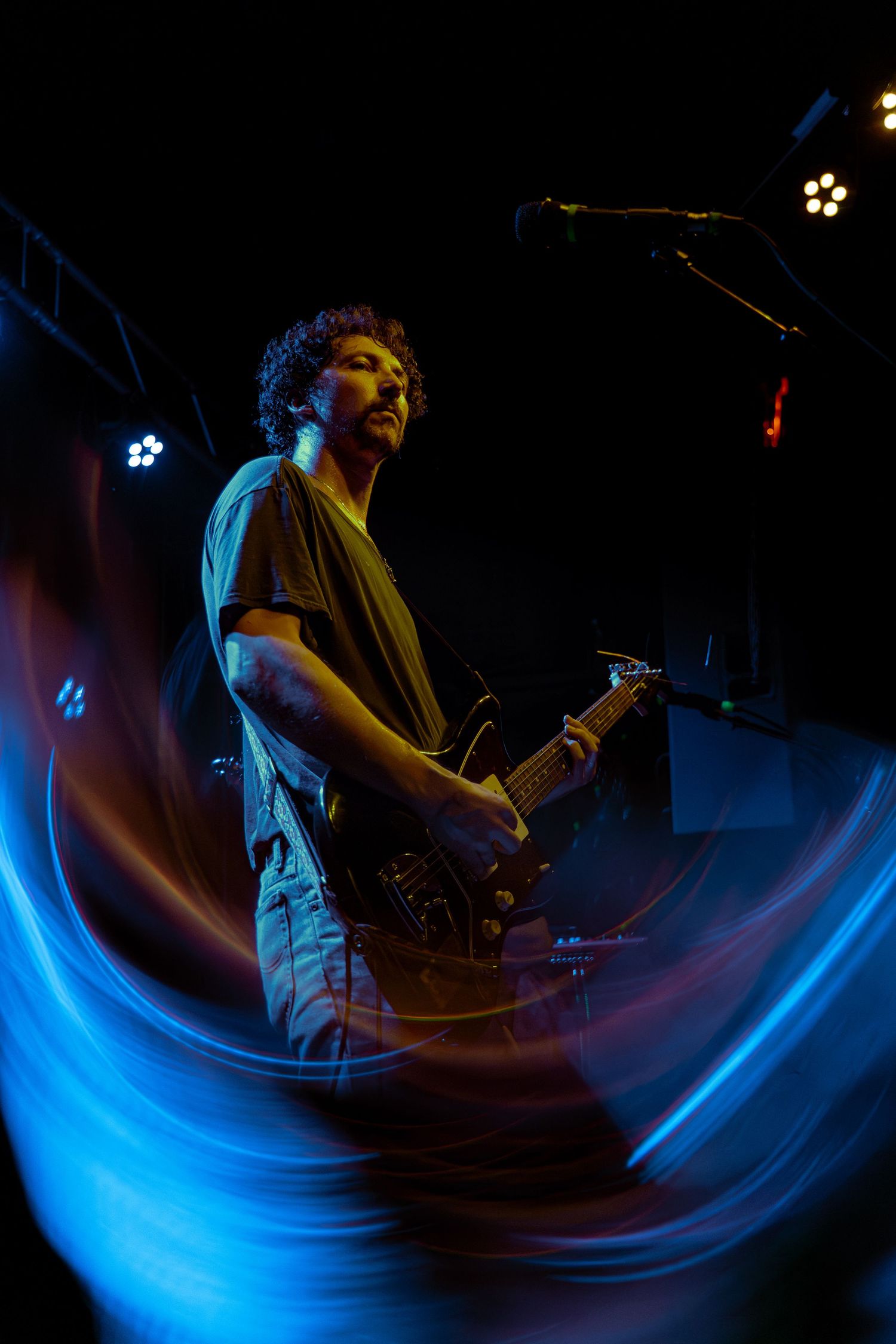 Four dynamic concert photos showcasing a musician performing with electric guitar lit by dramatic blue stage lighting effects.