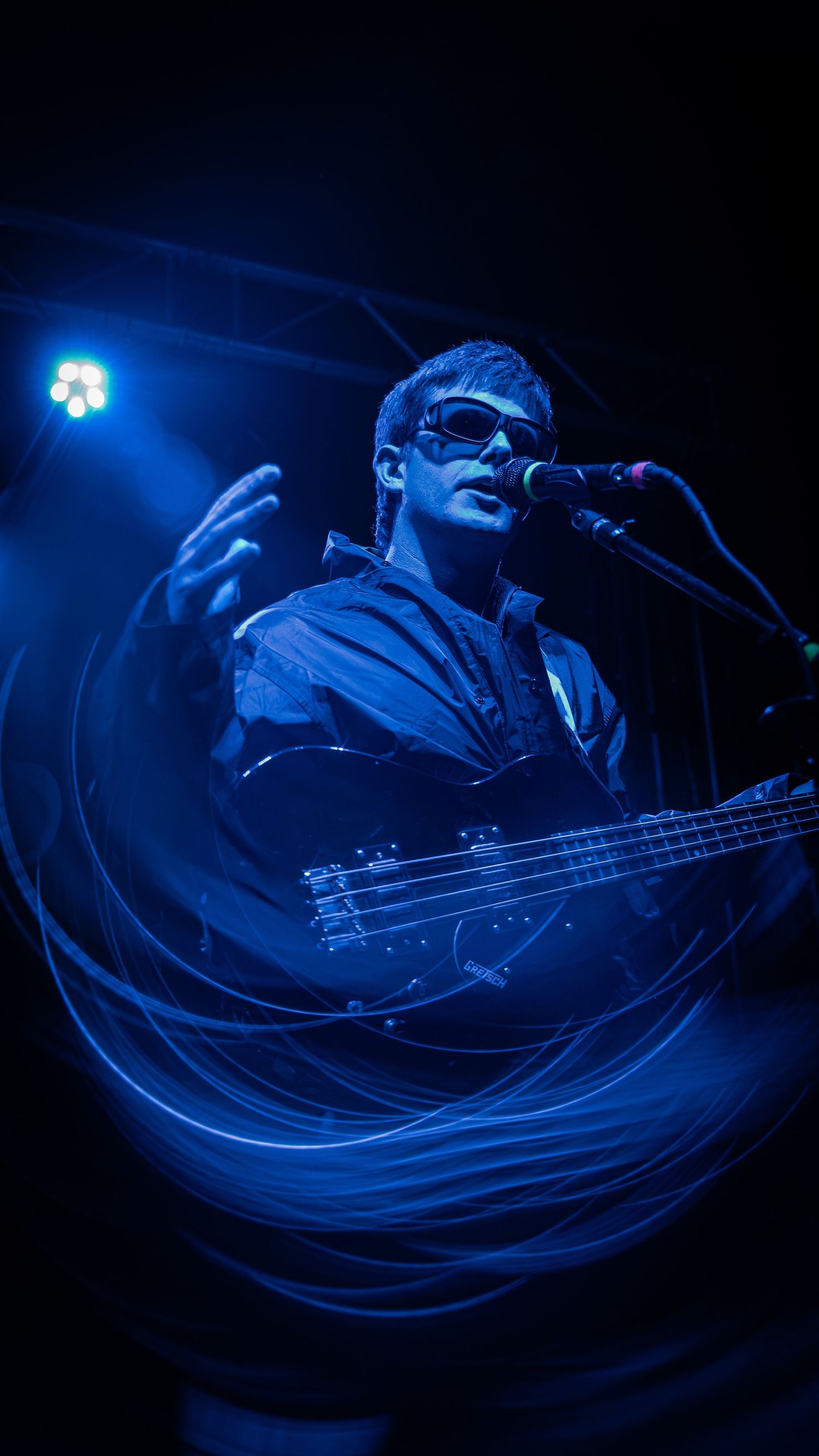 A bass guitarist performs on stage illuminated by dramatic blue lighting with a long exposure creating light trails effects.