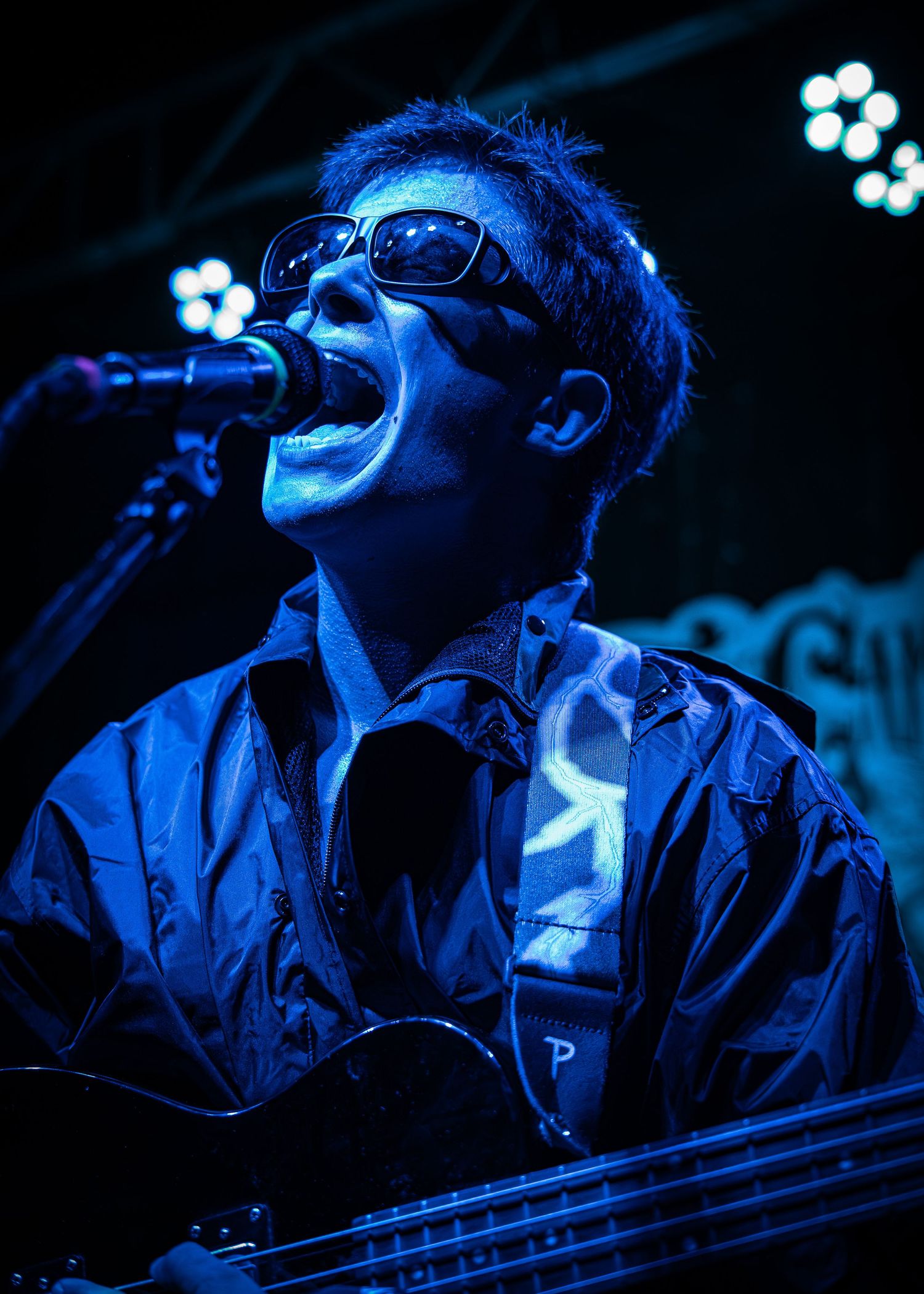 A passionate performer sings into a microphone under dramatic blue lighting during a concert performance.