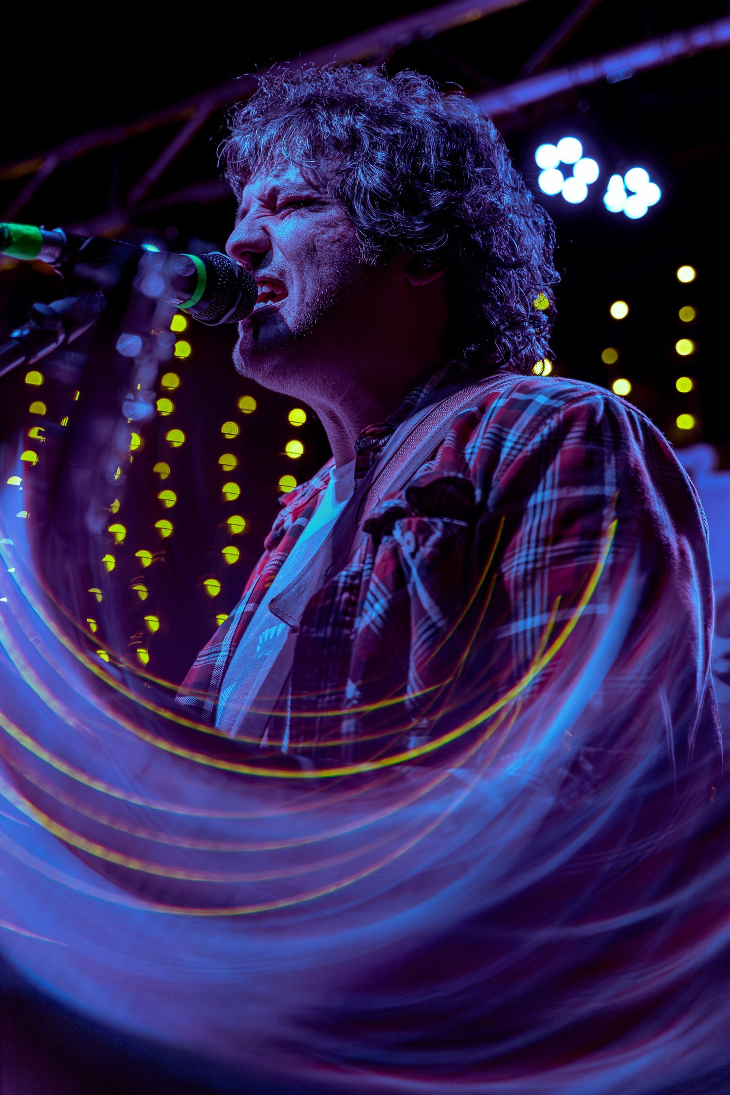 A closeup concert performance shot with swirling blue light trails and glowing yellow dots in the background.