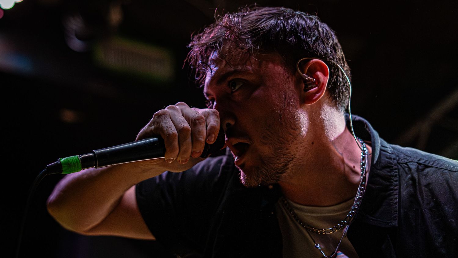 A performer in black sings passionately into a microphone on a darkened stage during a concert performance.