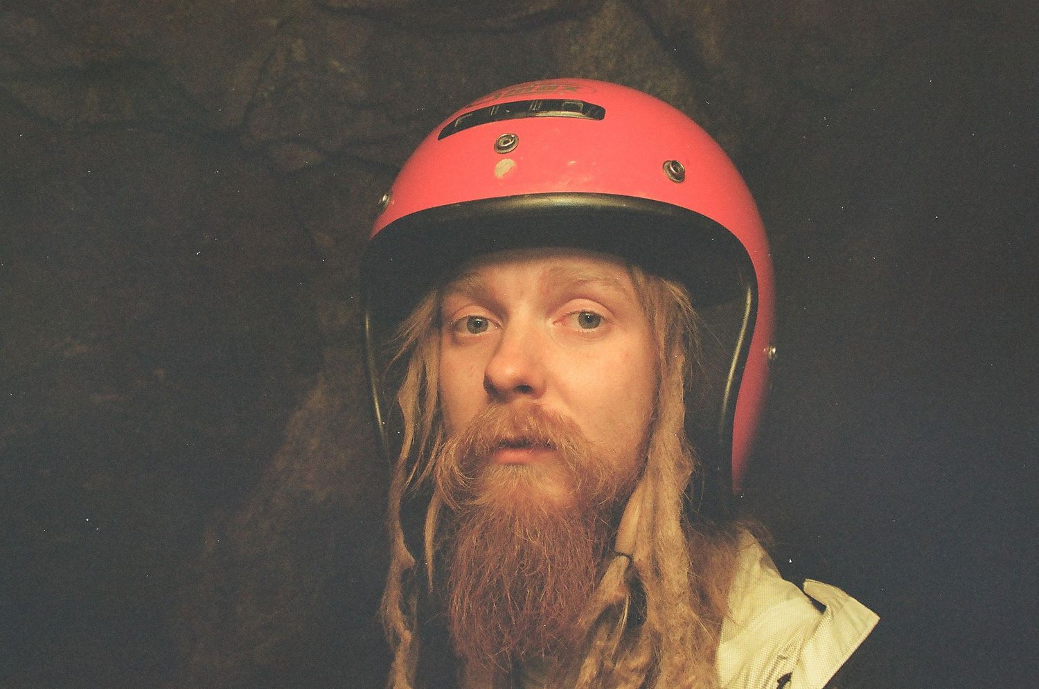 Person wearing a red baseball cap and beard photographed against dark background.