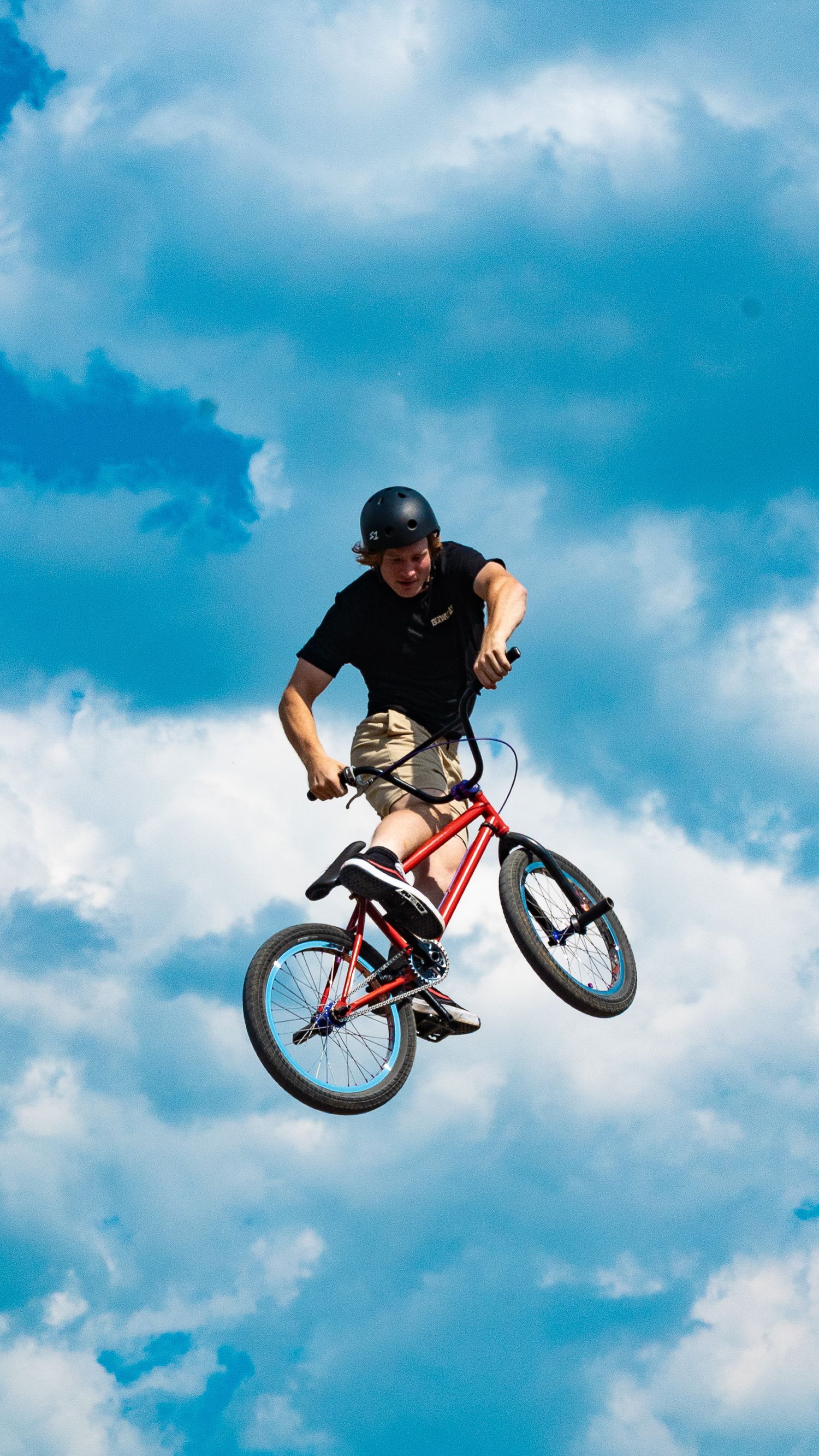 BMX biker jumps high performing freestyle trick with vibrant blue sky background.