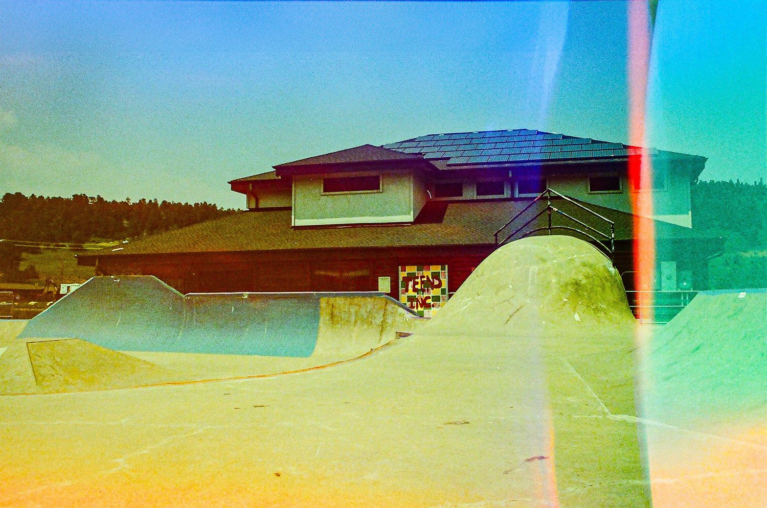 Skate park ramp against blue sky with light leak effects creating a dreamy vintage atmosphere.