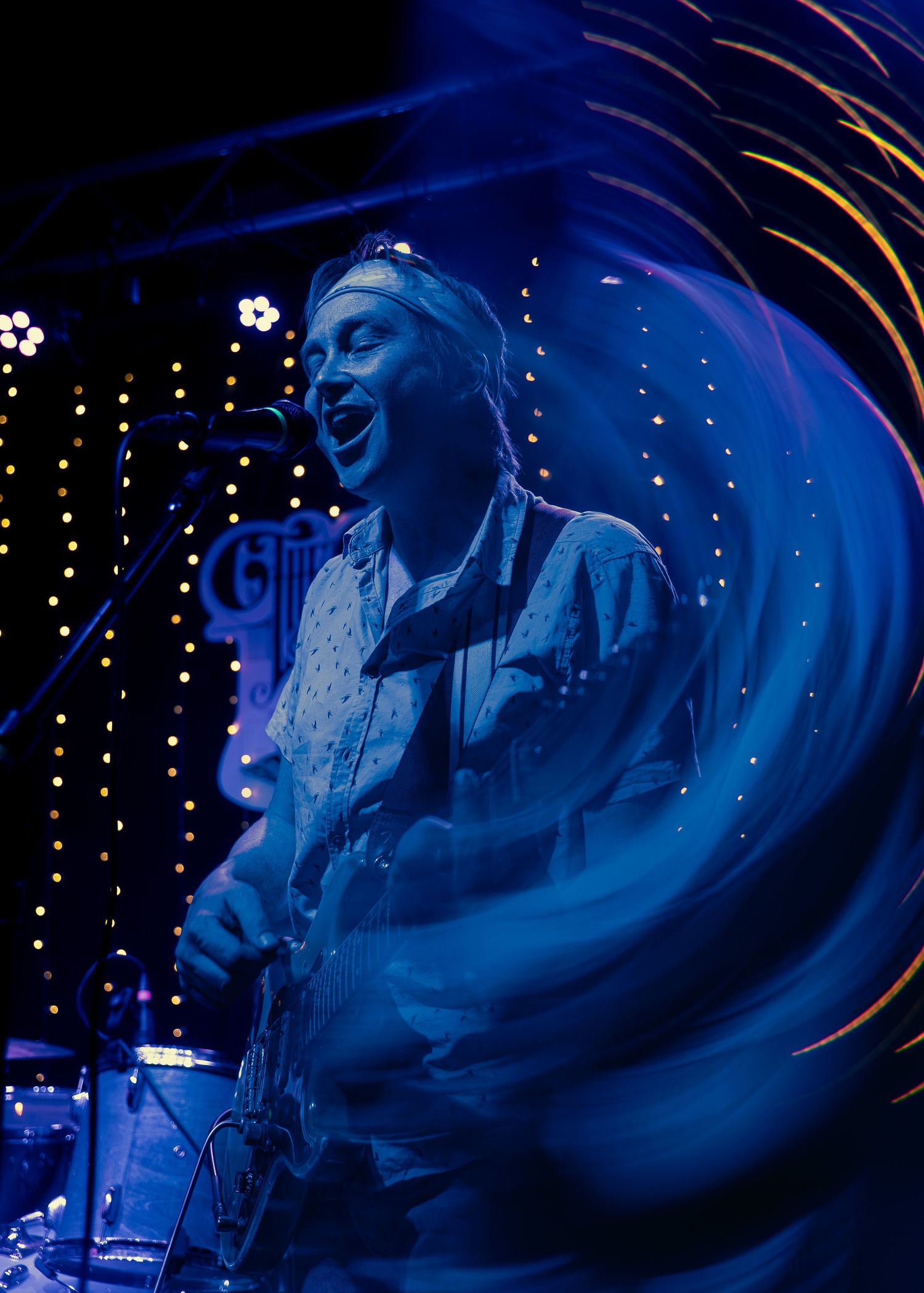 A performer sings passionately on stage under dramatic blue lighting during a live music performance at night.