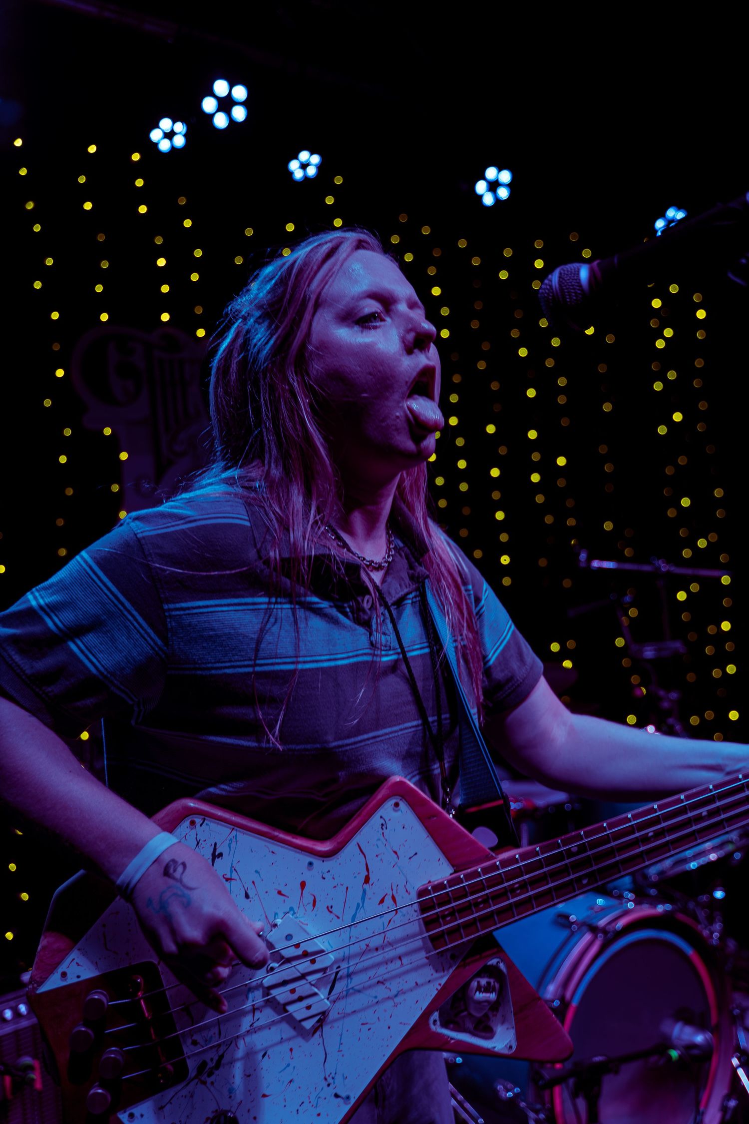 Musician playing bass guitar on stage with blue lighting and decorative flower lights in the background.