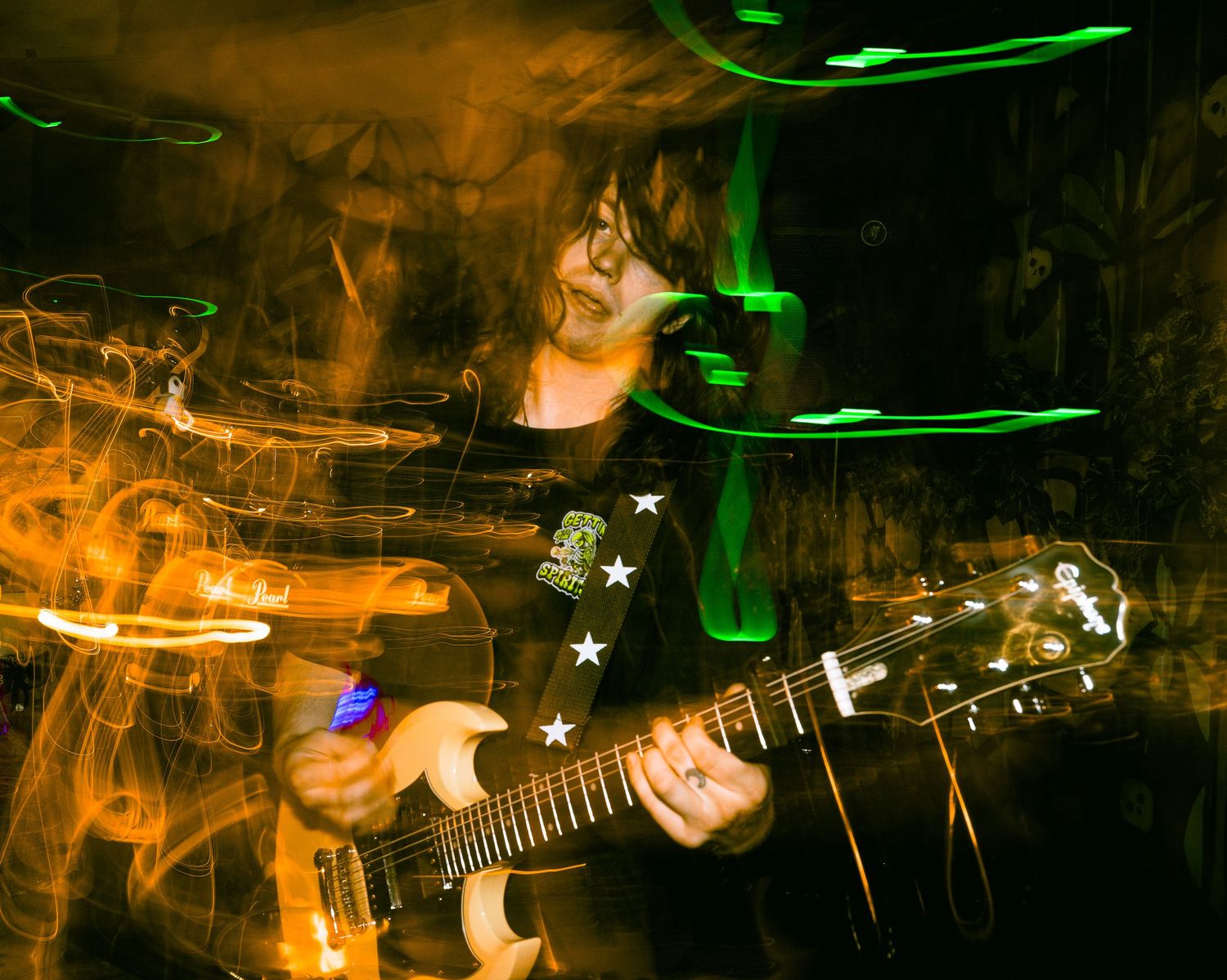 Concert performance captured with orange lighting and green light trails creating artistic effect.