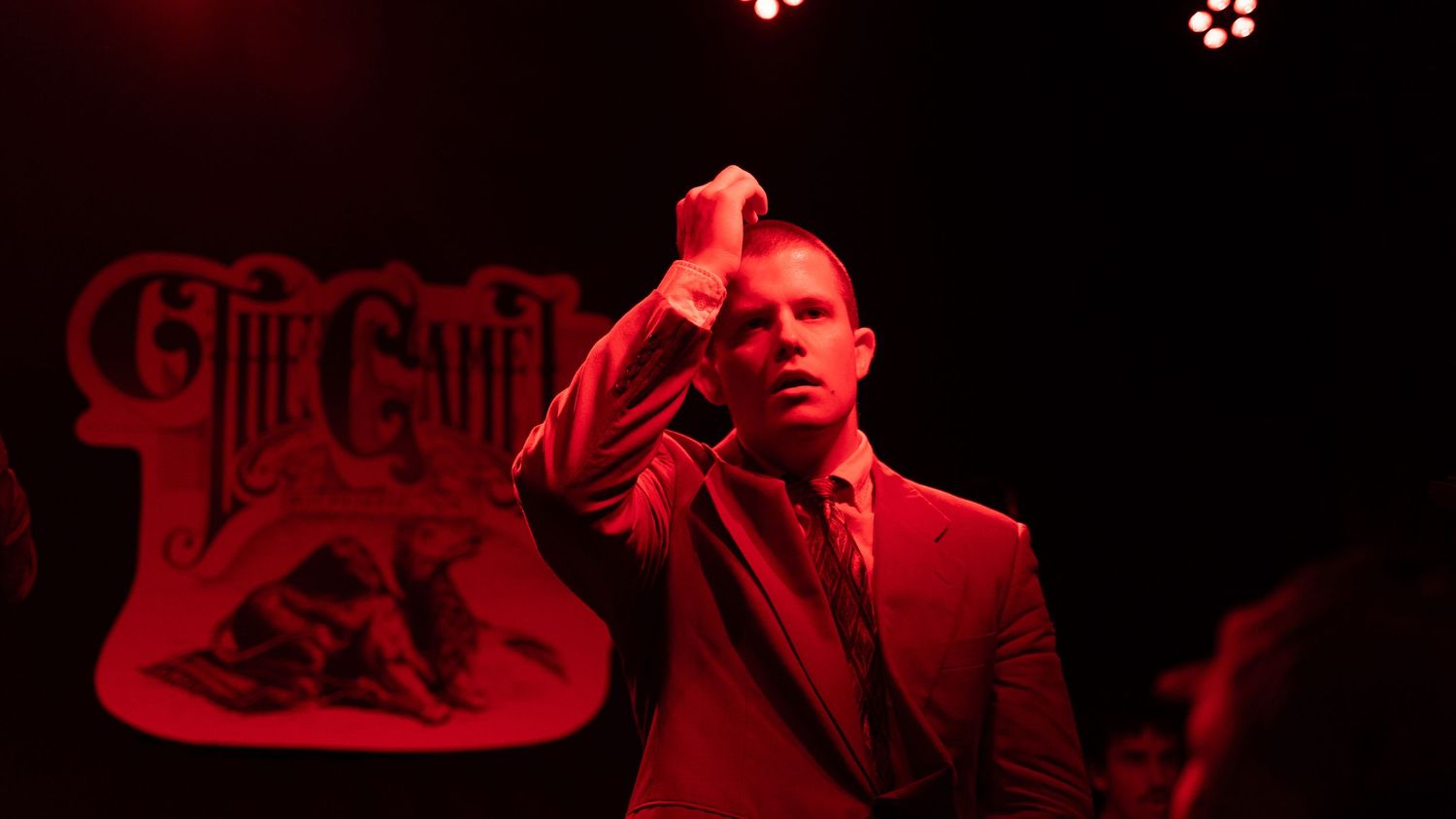 Musician performing under dramatic red stage lighting with band logo visible in background.