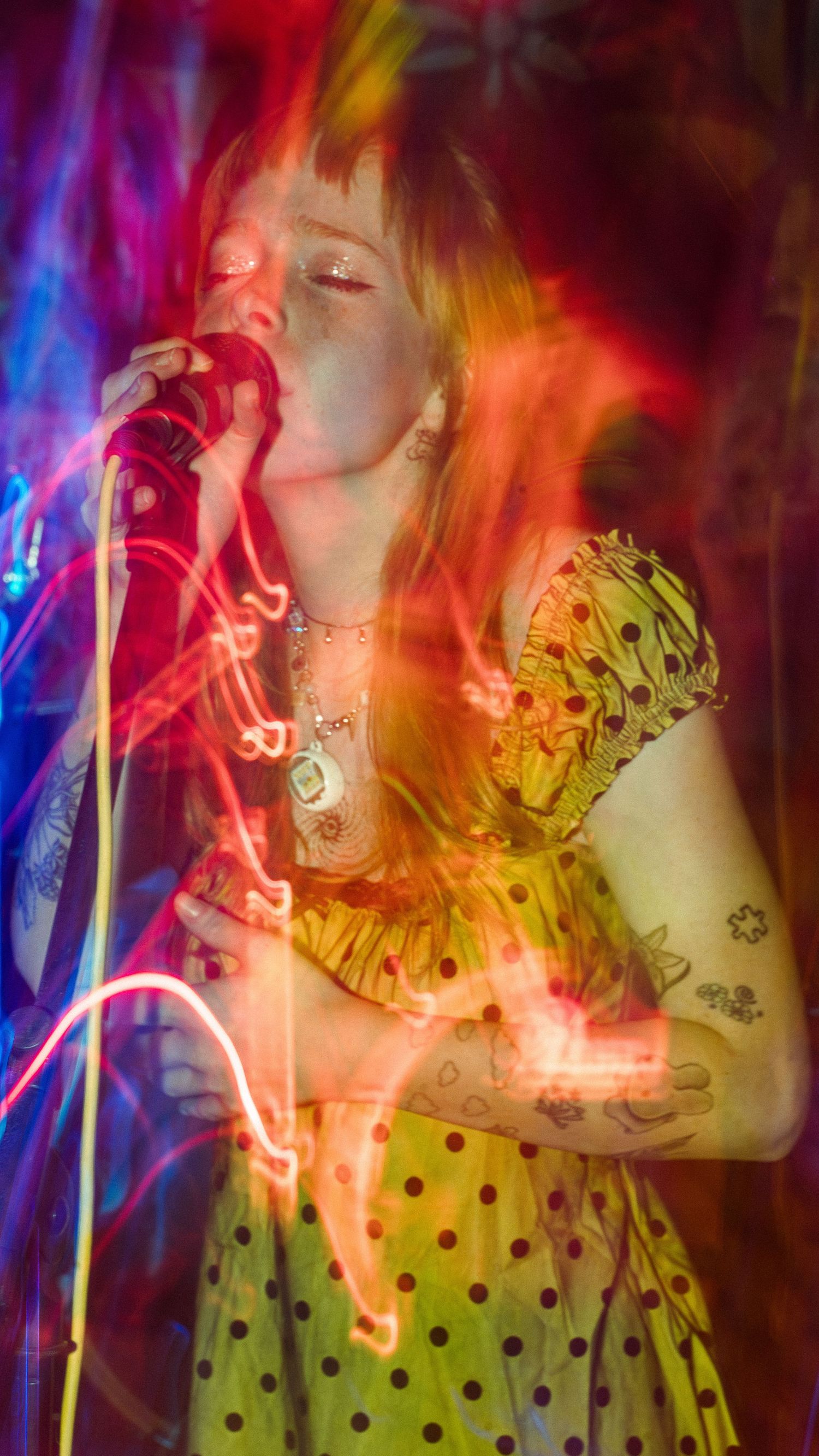 Singer performing in a polka dot dress with vibrant multicolored stage lighting creating a dream-like effect.