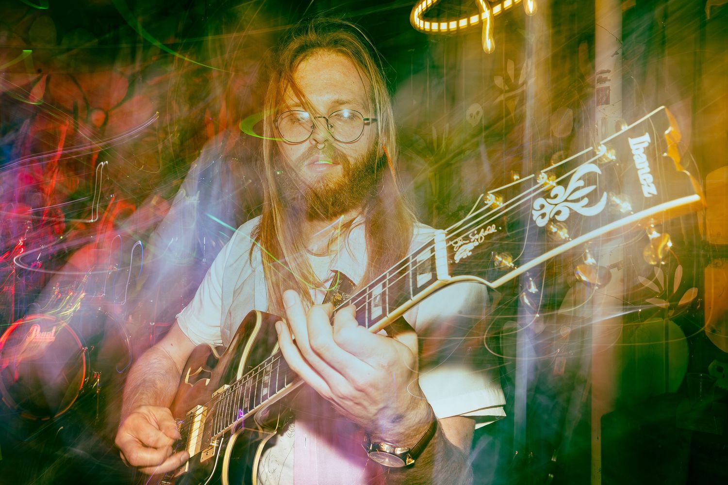 Guitarist with long hair playing electric guitar under colorful stage lights with double exposure effects.