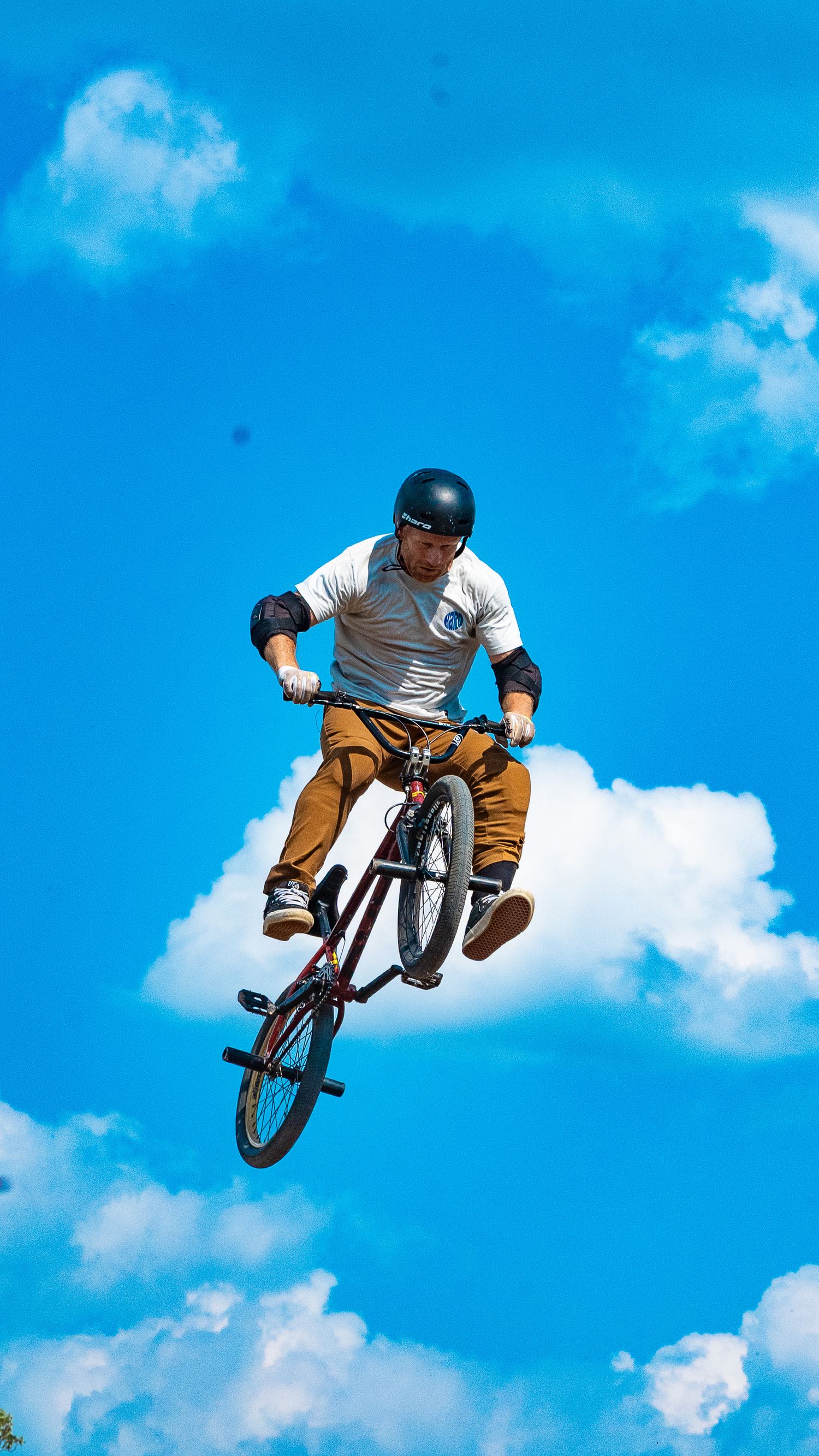 BMX athlete performs mid-air trick with bike against bright blue sky and clouds.