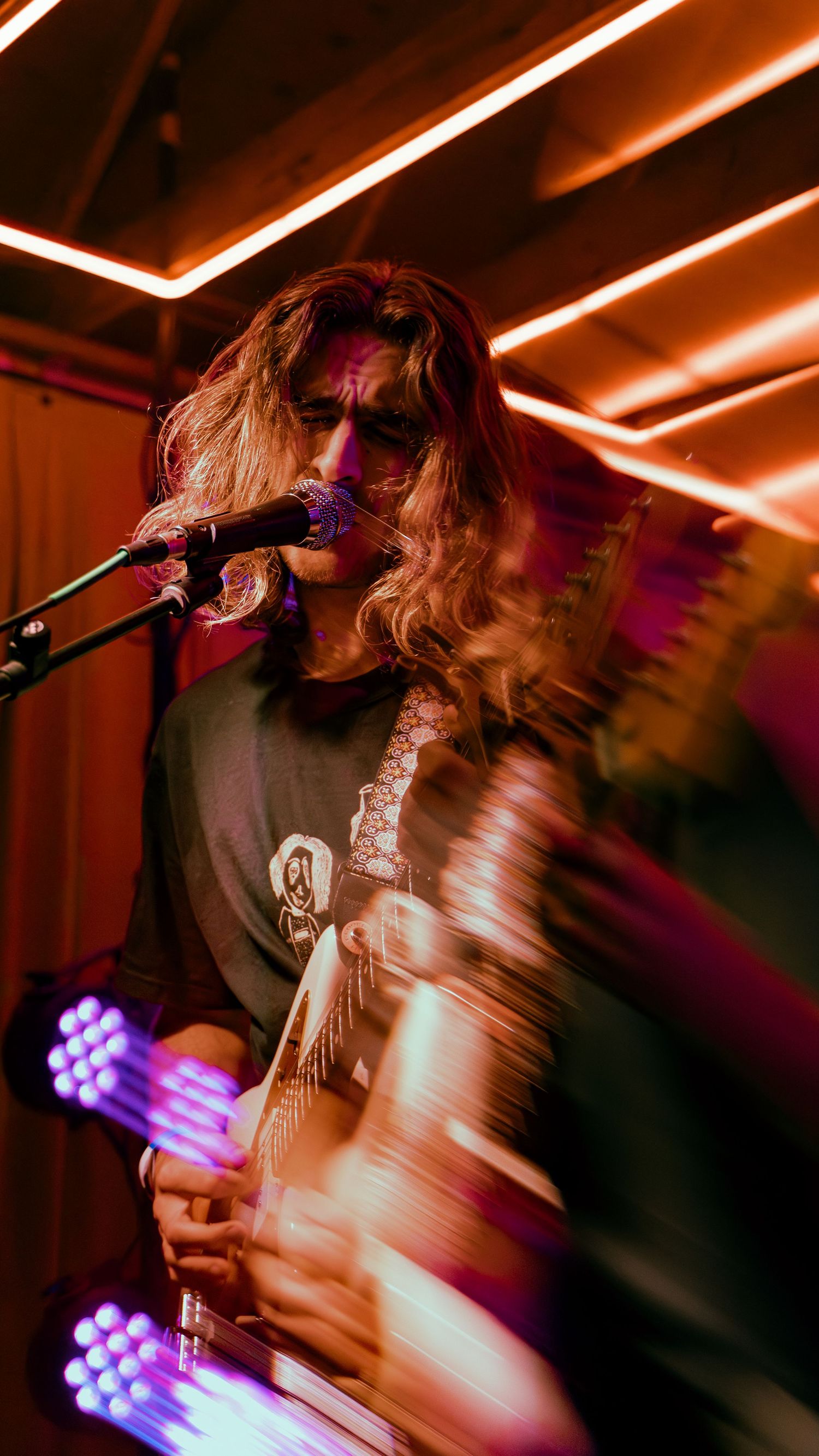 Musician performing on stage with blurred motion effect under red and purple lighting creating dynamic movement.