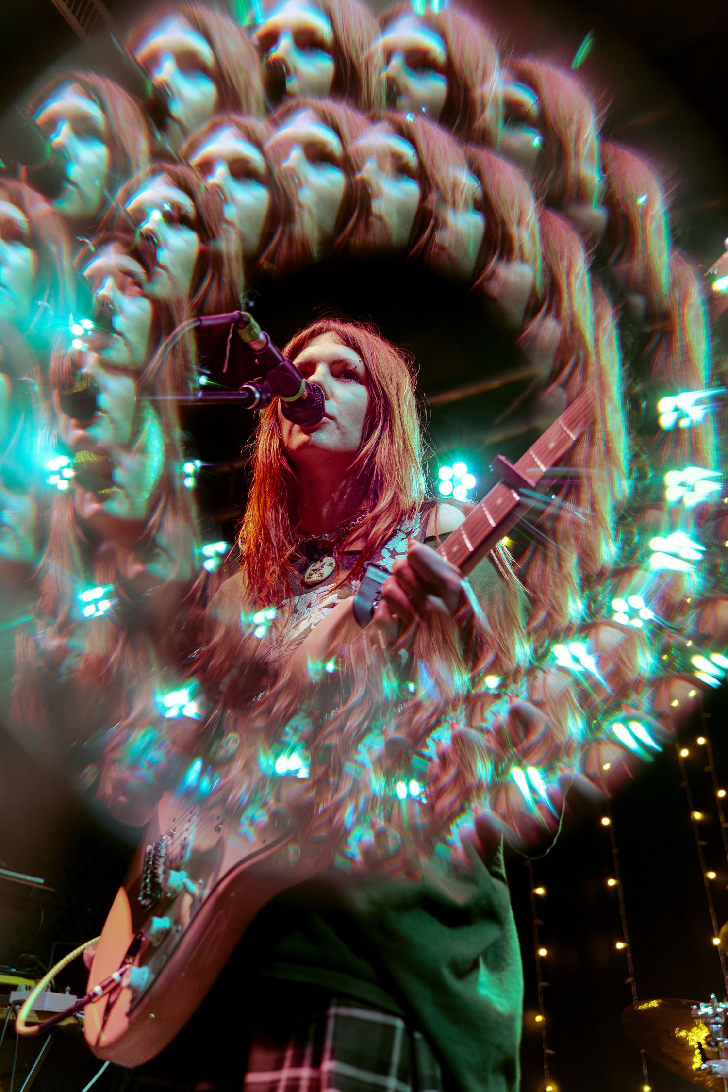 Concert performer with colorful hair passionately playing in dramatic lighting with blue and green stage effects.