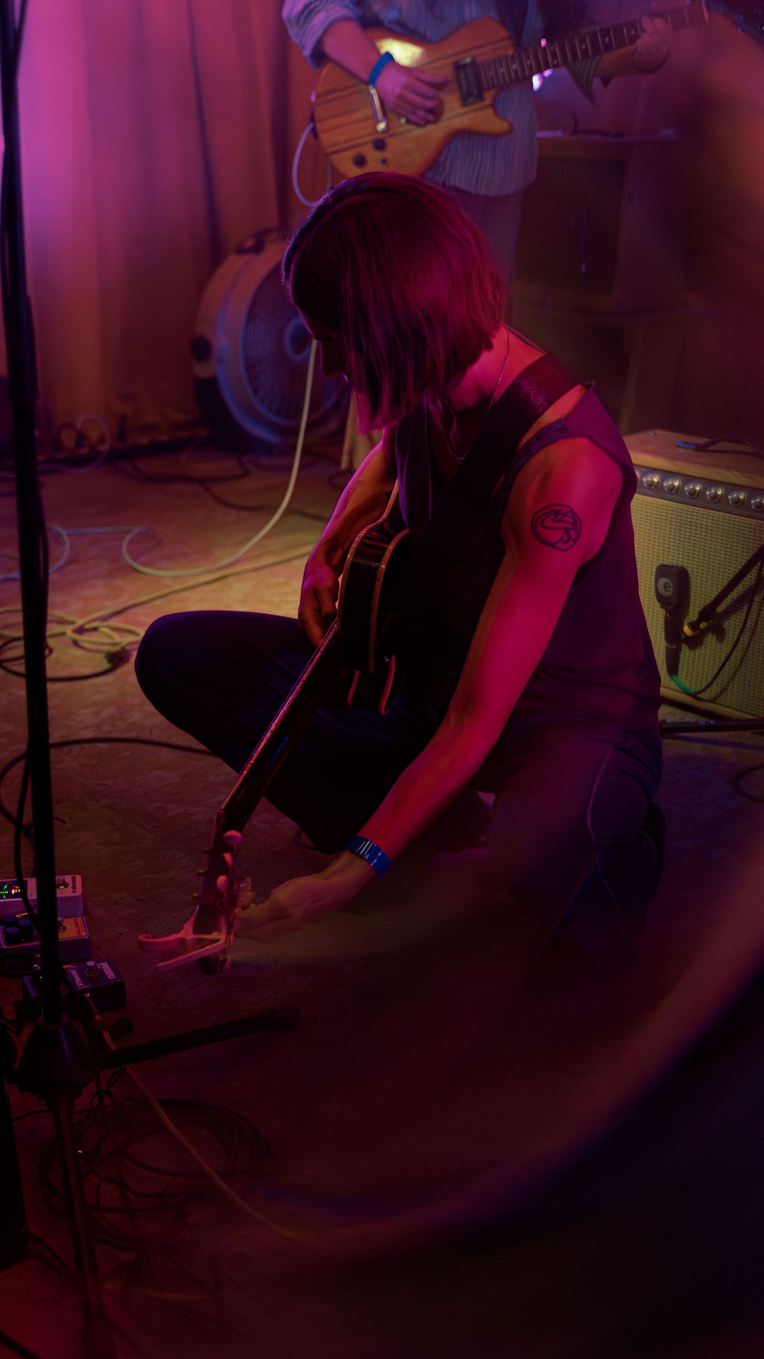 Musicians perform on stage under moody purple lighting at a live concert venue.