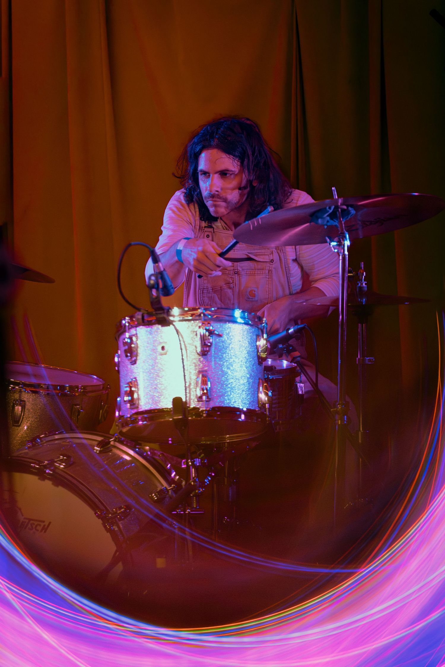 Drummer performs on stage with dramatic pink and blue lighting creating an artistic motion blur effect.