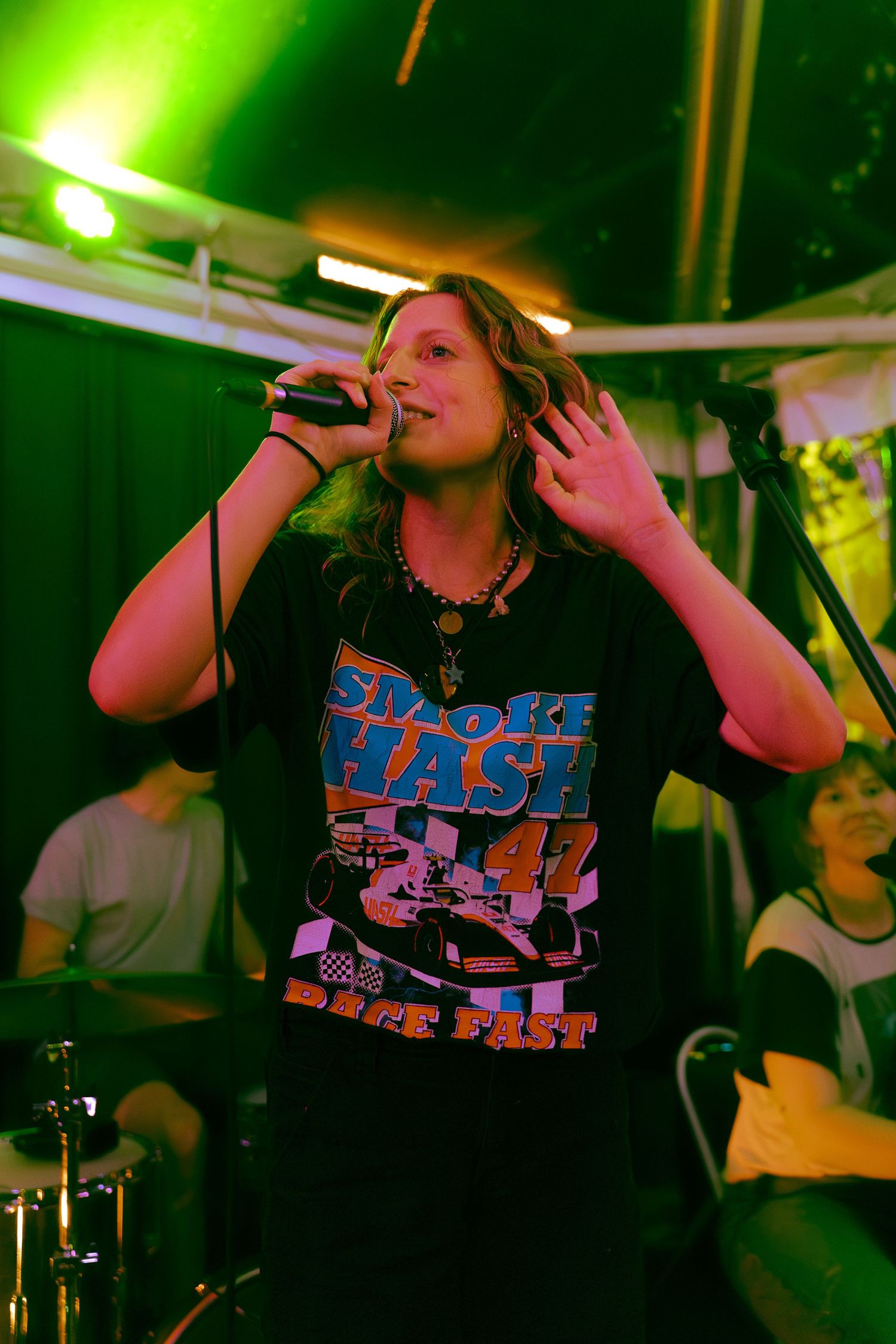 Multiple concert photos show a performer in a black graphic t-shirt singing on stage under green lighting.
