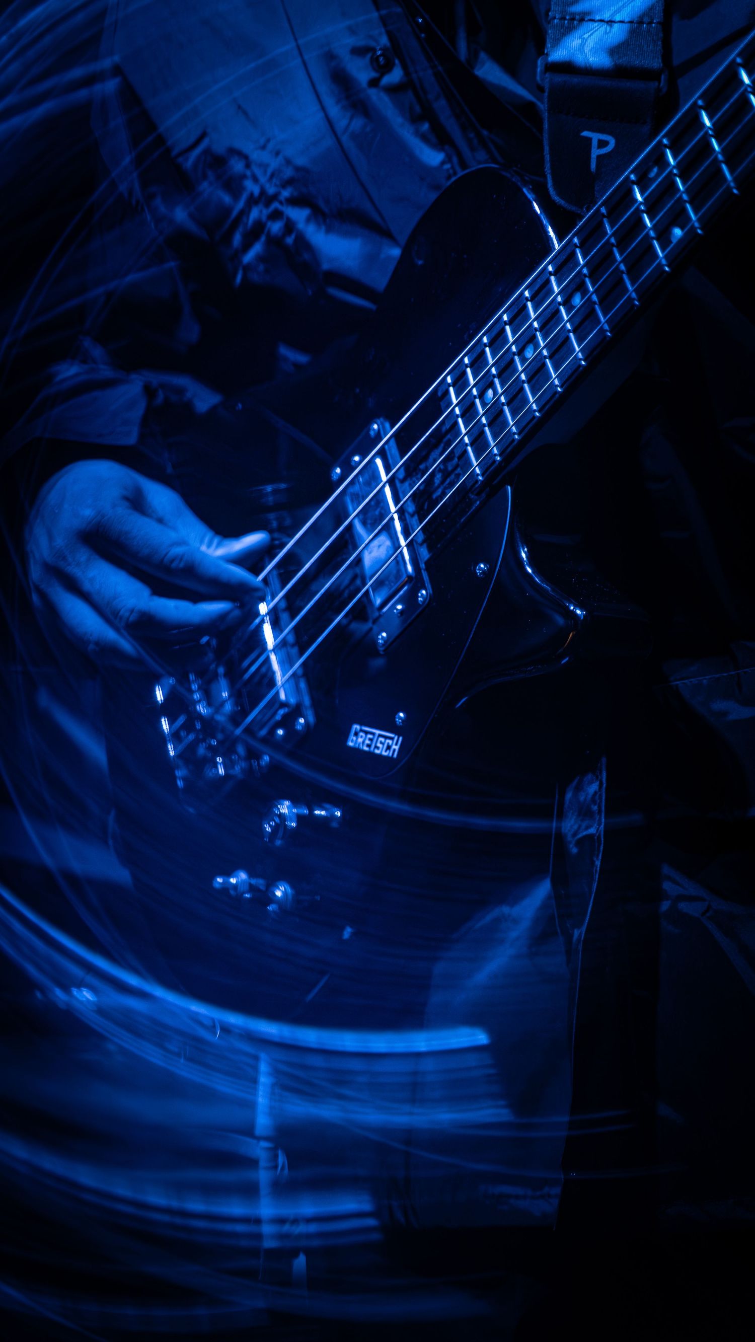 Motion blurred electric bass guitar lit in deep blue stage lighting creating dramatic streaks during performance.
