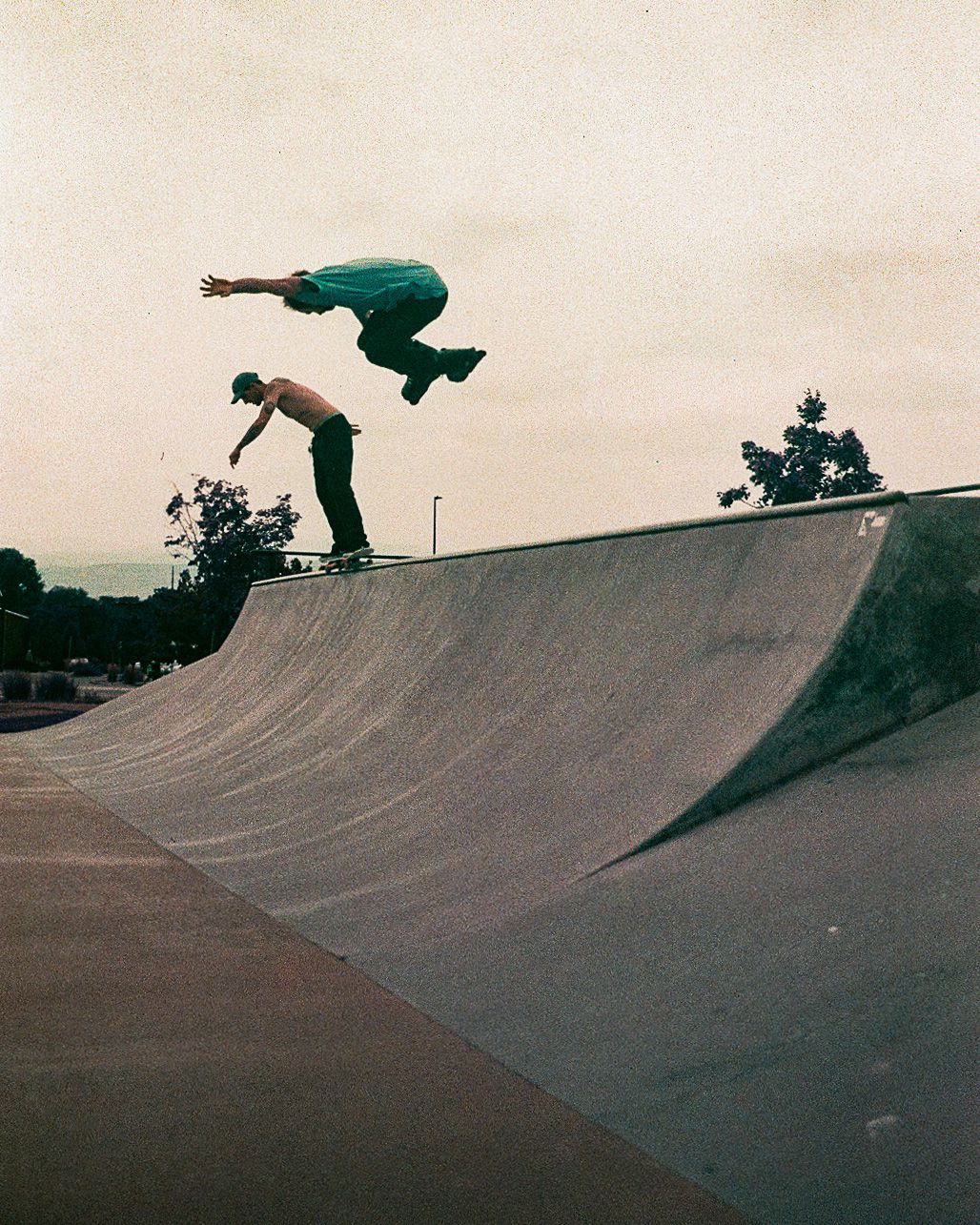 Skateboarder performs an aerial trick on a curved halfpipe ramp at sunset.