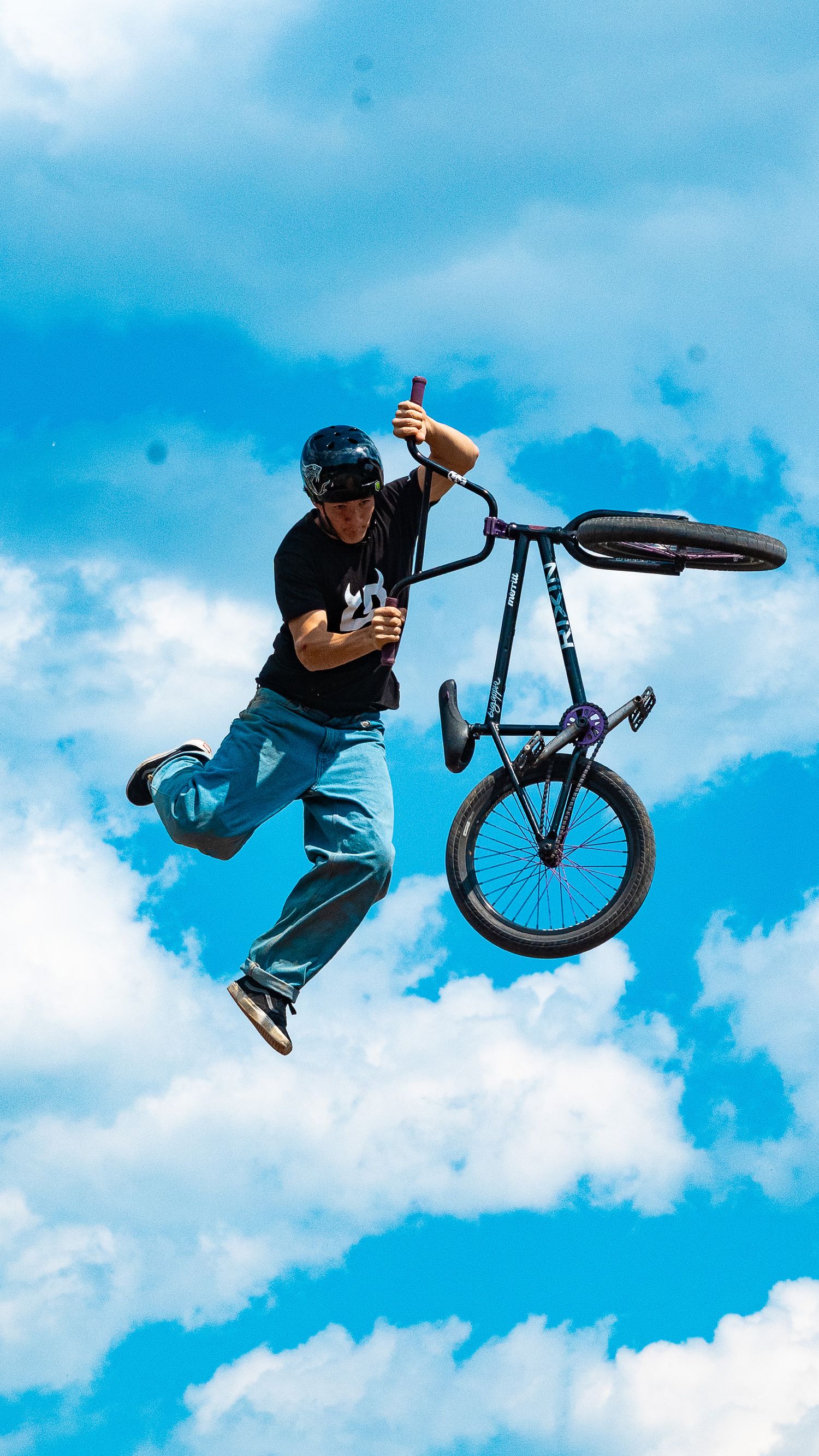 Rider separates from BMX bike during dramatic aerial stunt against blue sky.