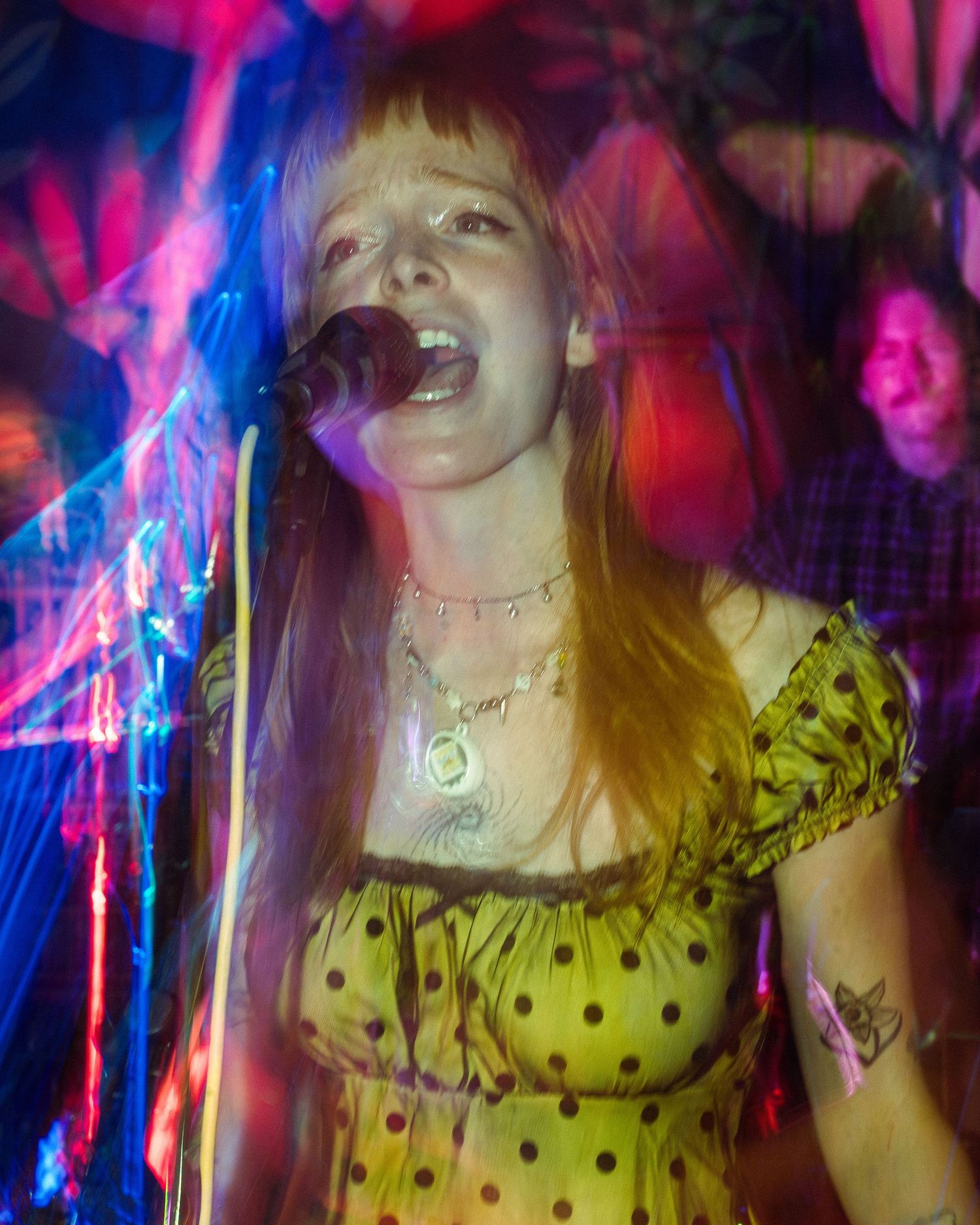 Concert performer in polka dot dress singing passionately under vibrant pink and blue stage lighting.