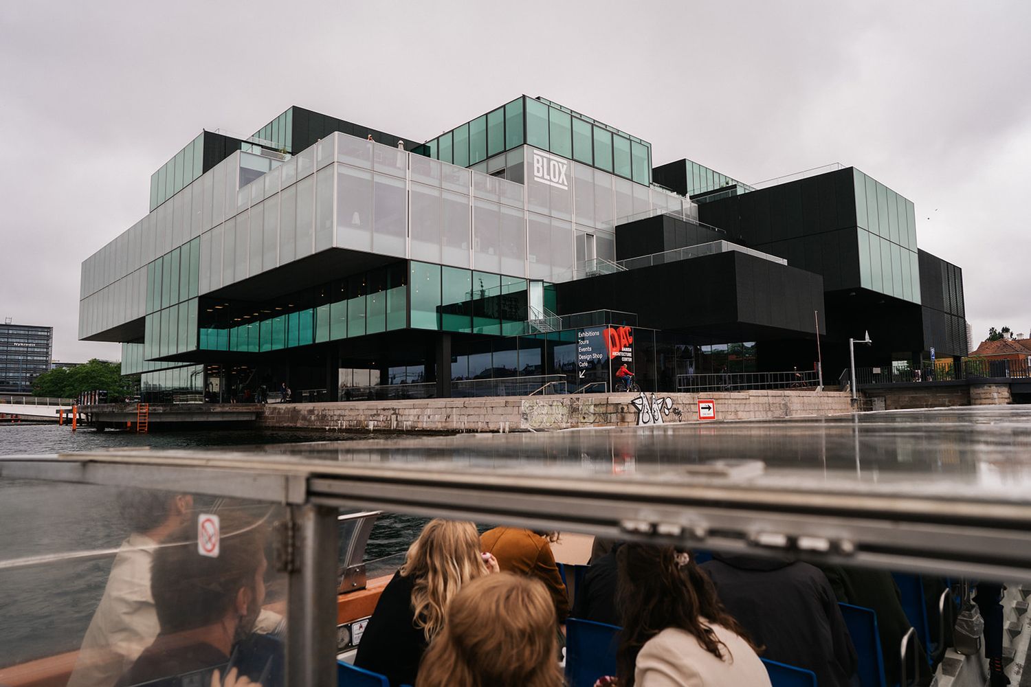 Modern black and glass architectural building with geometric shapes viewed from street level on a cloudy day.