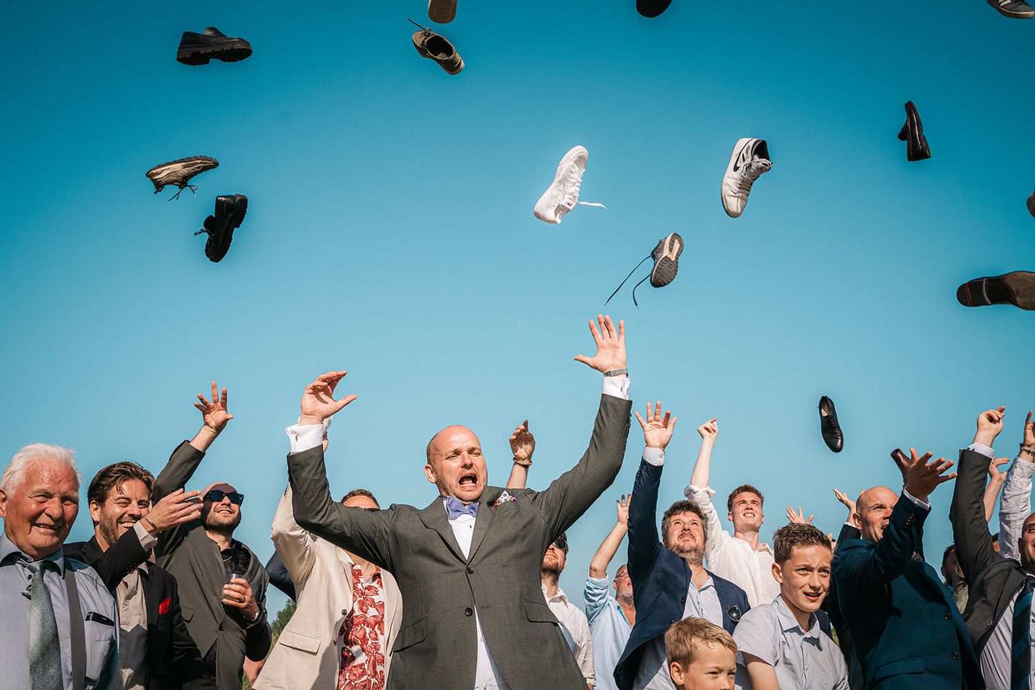 Dress shoes suspended in mid-air against bright blue sky during celebration.