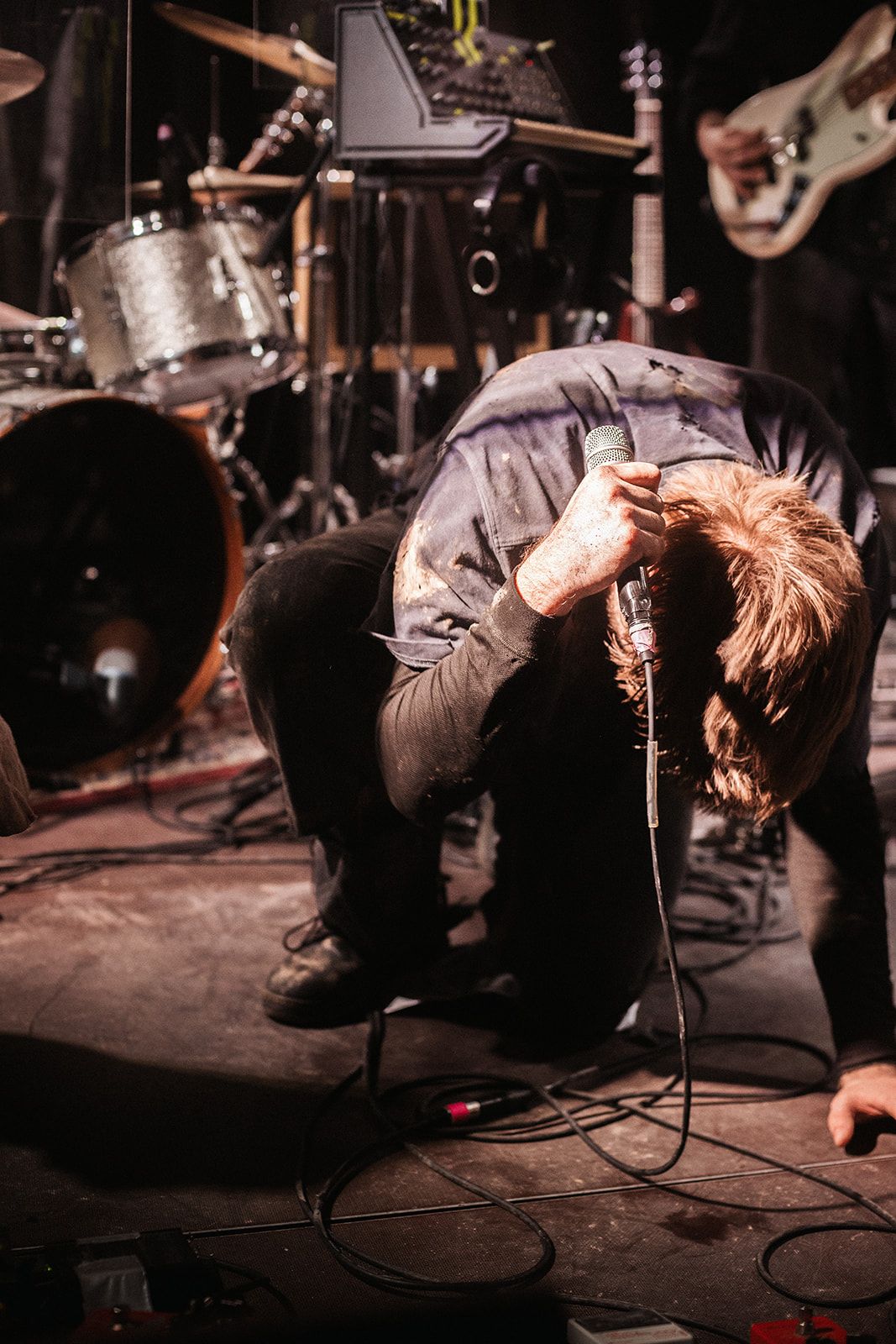 Concert performer energetically bends backwards on stage during an intense live music performance at a dark venue.