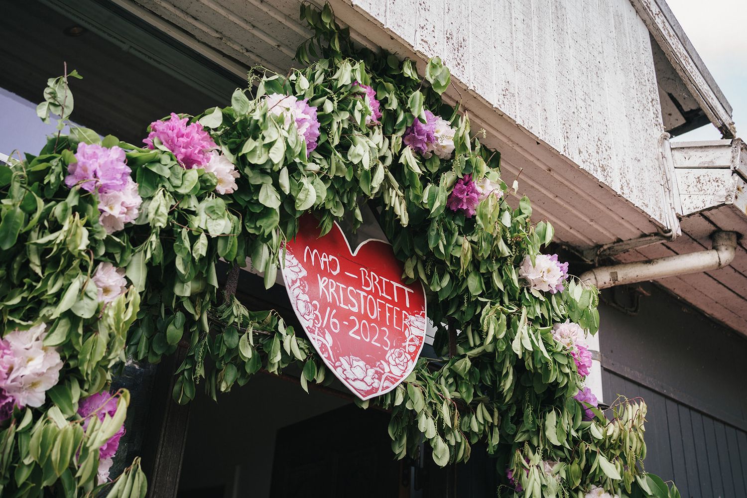 Pink flowers and greenery adorn a doorway with a decorative red heart sign hanging above.