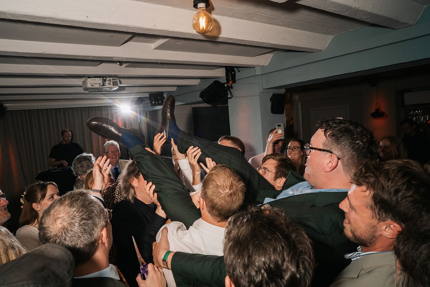 A crowded basement concert venue with hands raised in the air as patrons enjoy live music under dim lighting.